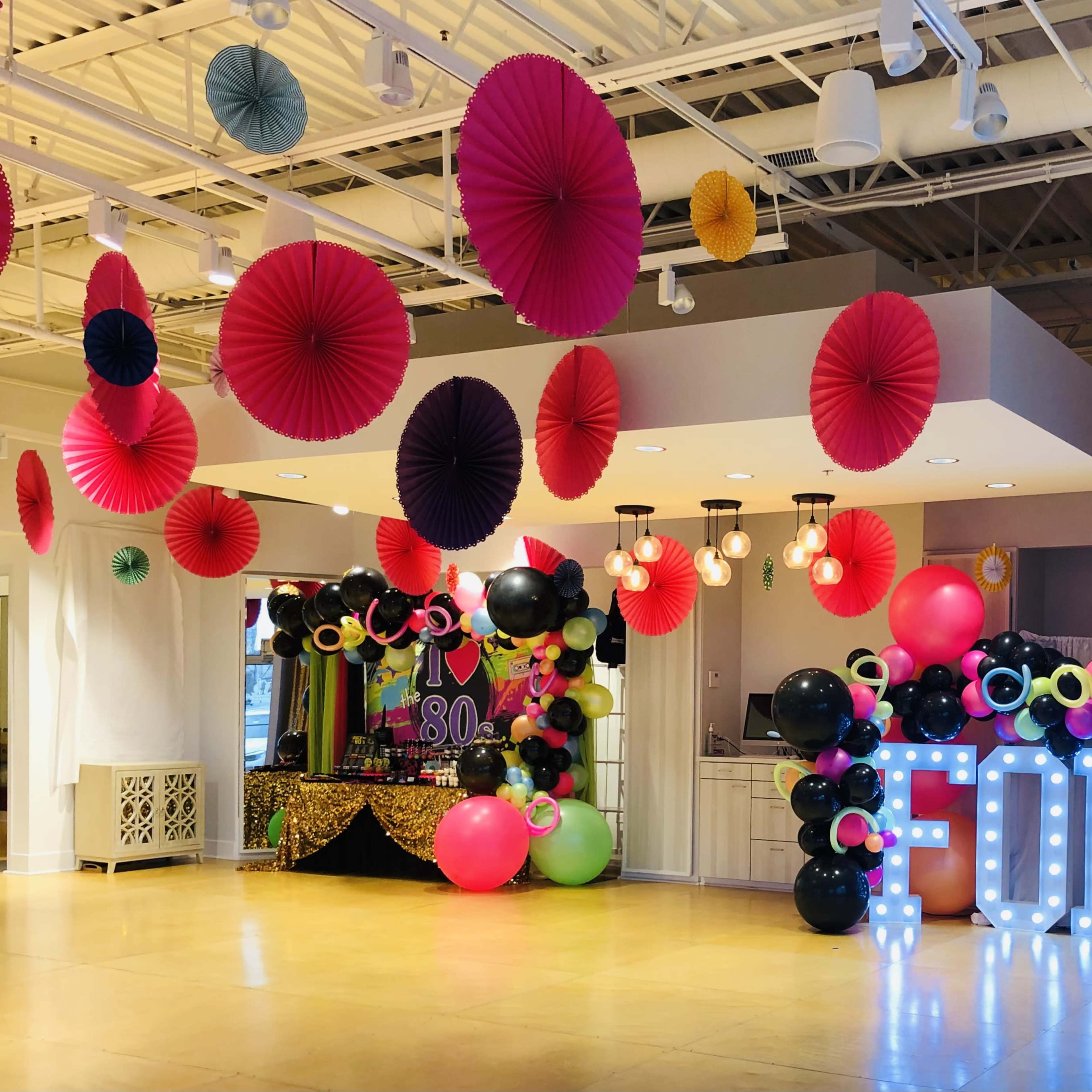 The scene features a decorated event space with colorful paper decorations, large balloons, and a light-up display spelling "FORTY."