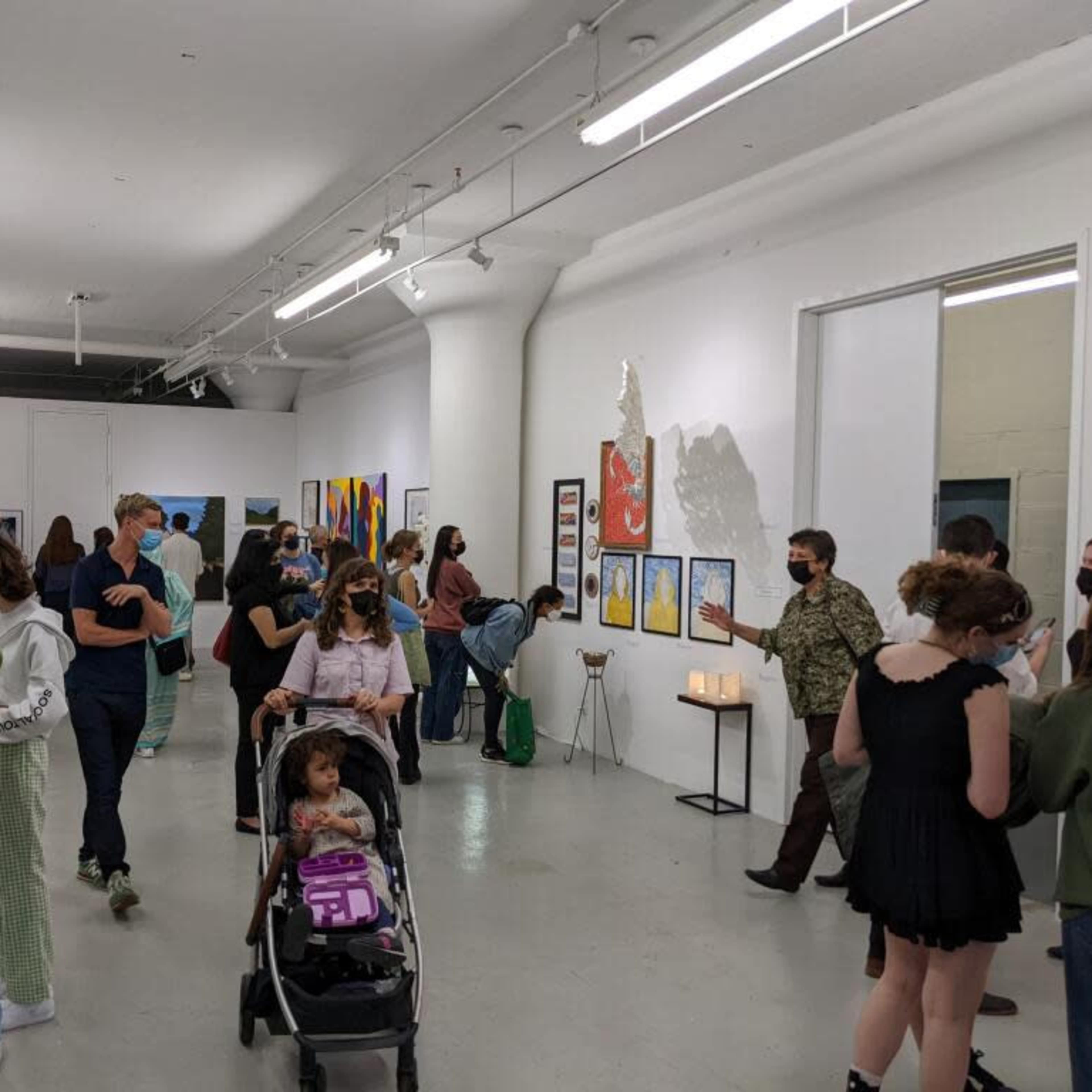 A group of people engages with artwork in a spacious art gallery, with several pieces displayed on the walls.