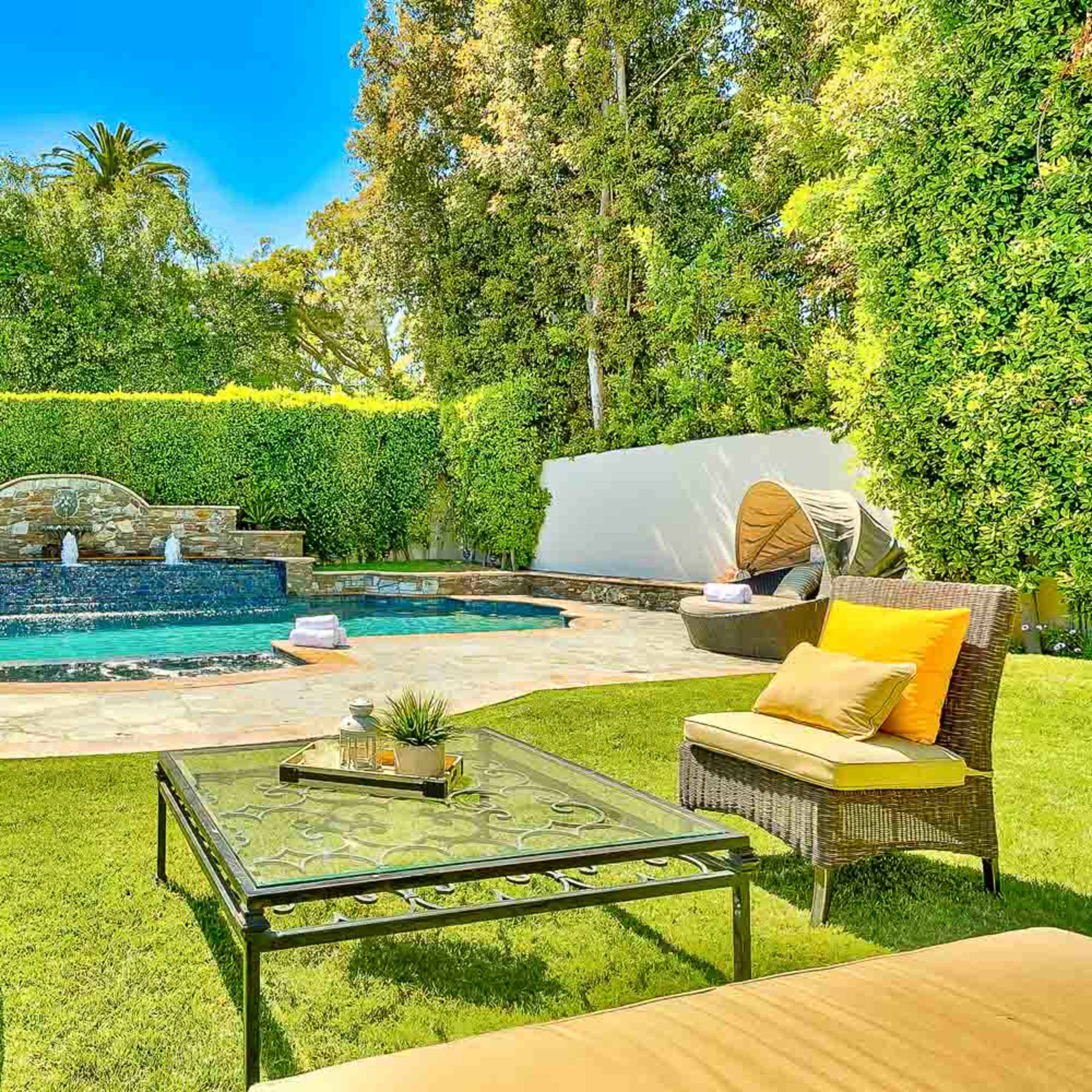 A landscaped backyard featuring a swimming pool with a stone waterfall, surrounded by lounge chairs and greenery.
