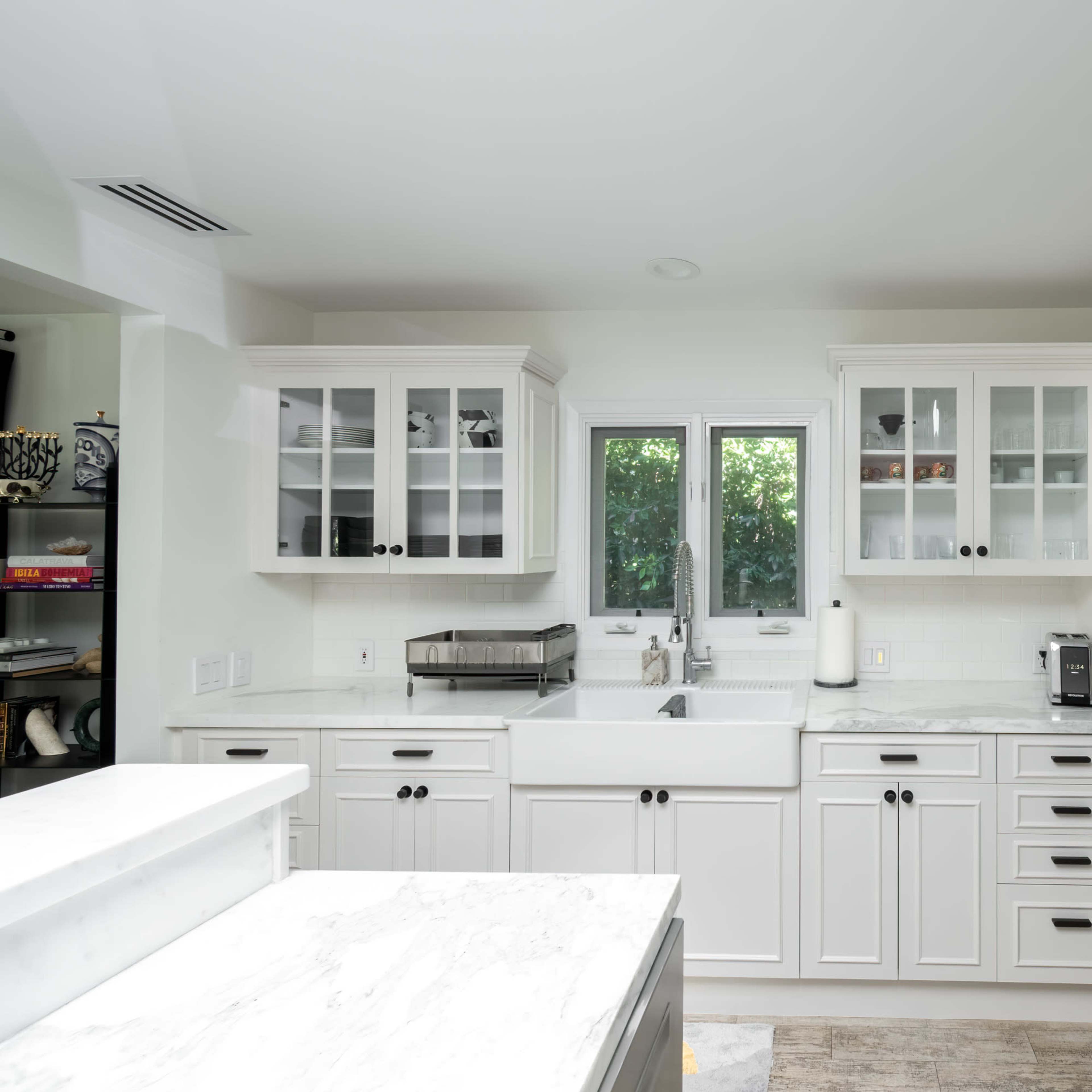 The kitchen features white cabinetry, a farmhouse sink, and stainless steel appliances, with a window providing natural light.