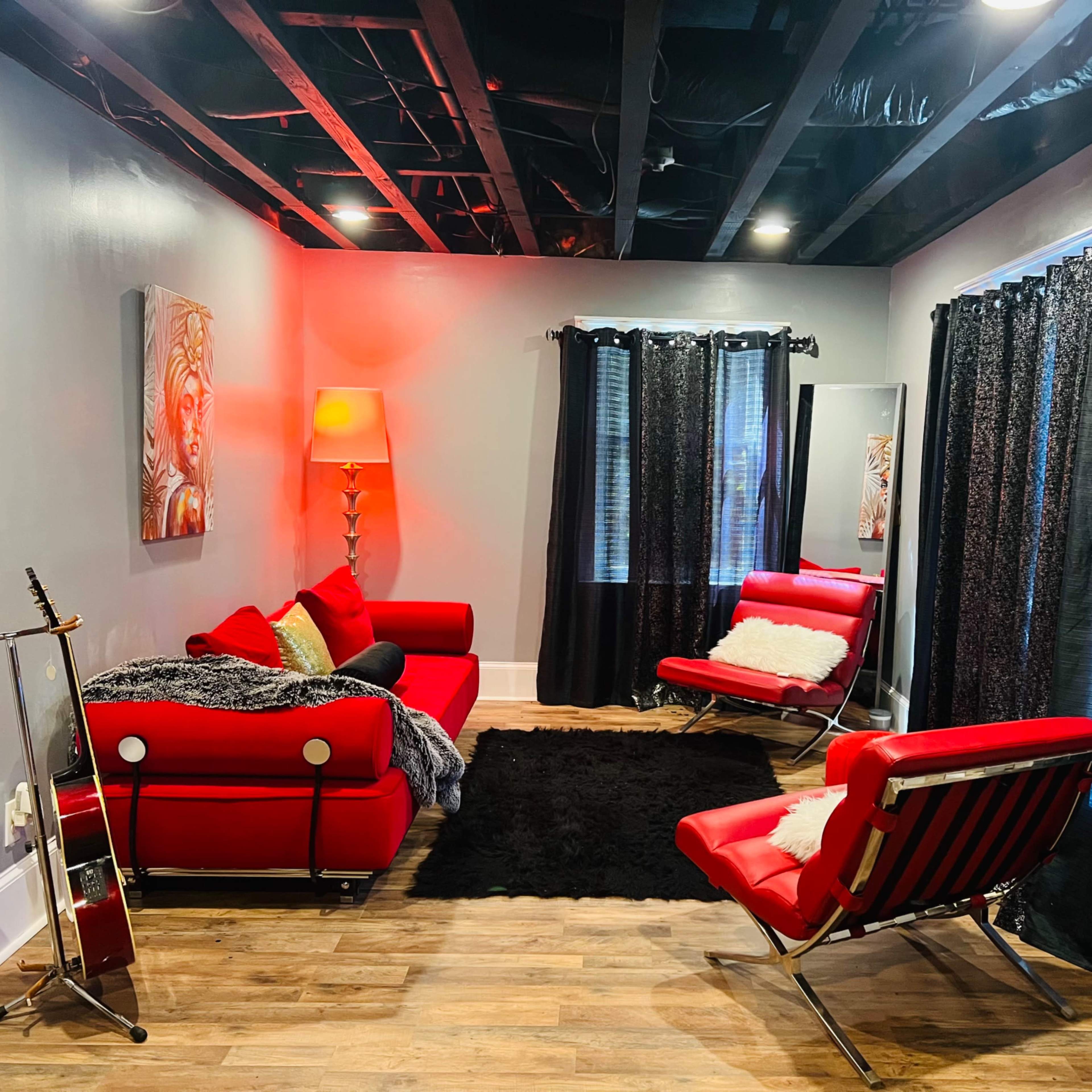 A modern living room with red furniture, including a sofa and chairs, black curtains, and a wooden floor.