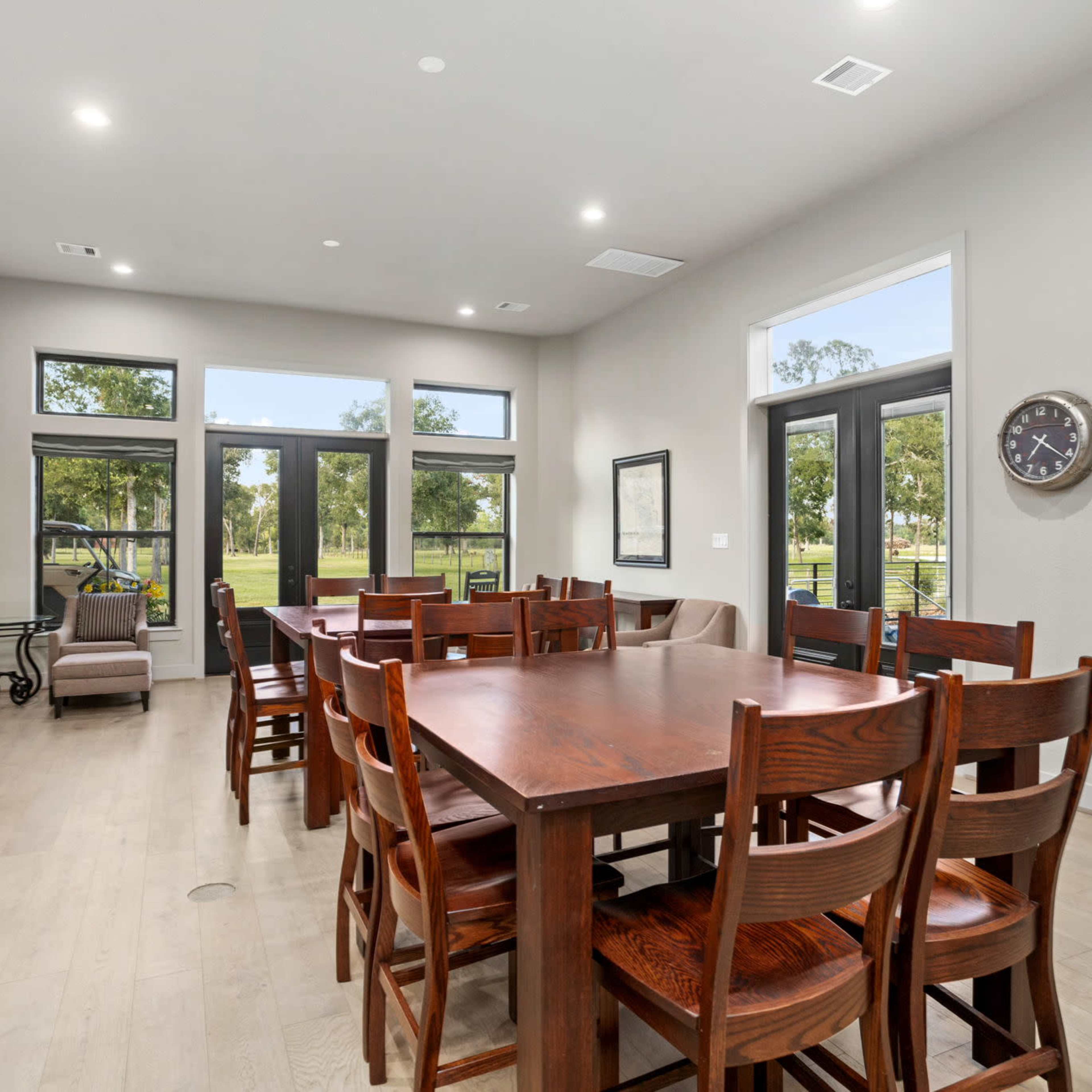A spacious, well-lit dining area with a large wooden table surrounded by chairs, adjacent to a living space featuring a sofa and large windows.