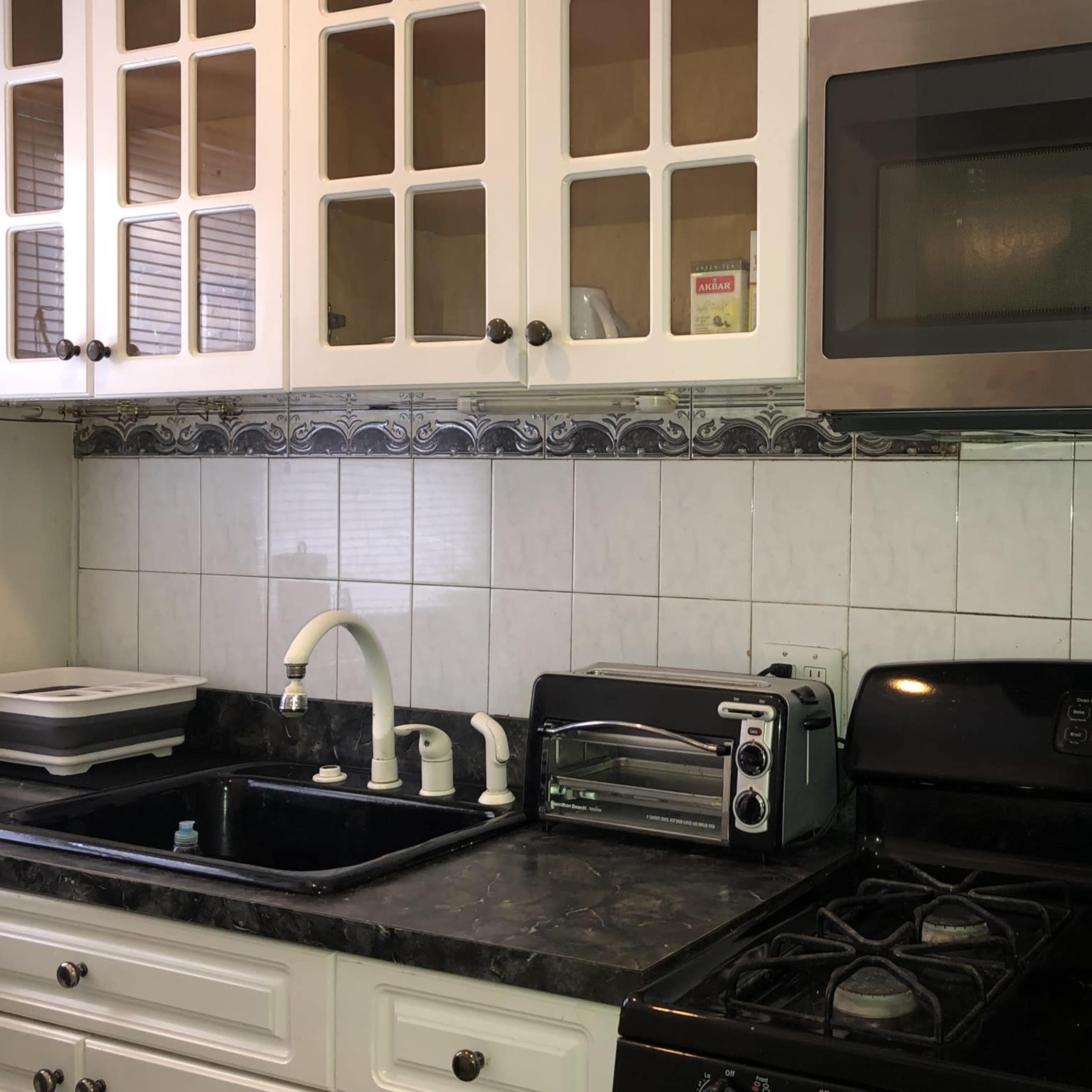 A kitchen counter with a black stove, a toaster oven, a microwave, a sink with a white faucet, and glass-front cabinets above.