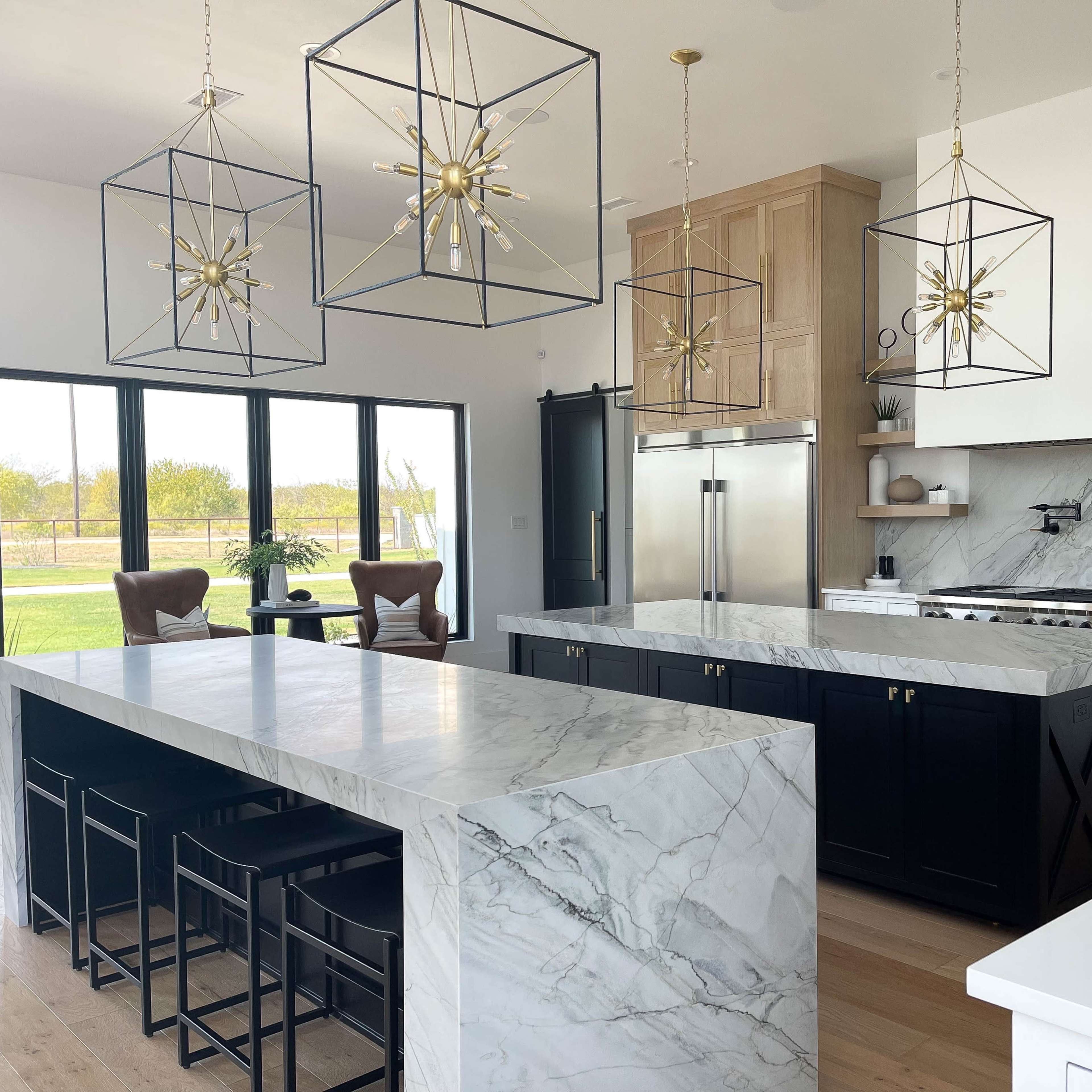A modern kitchen featuring a large island with marble countertops, stainless steel appliances, and pendant lighting.