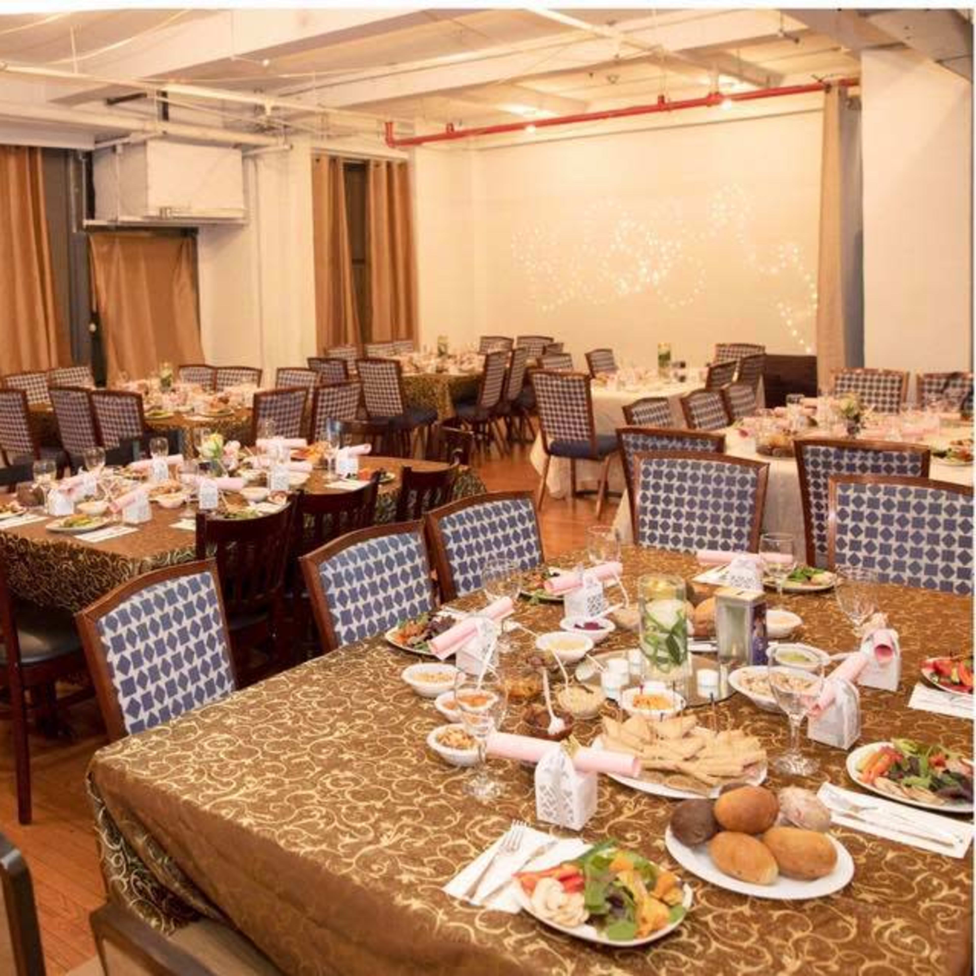 A banquet hall with multiple tables set for a formal dinner, featuring tablecloths, place settings, and a variety of food.