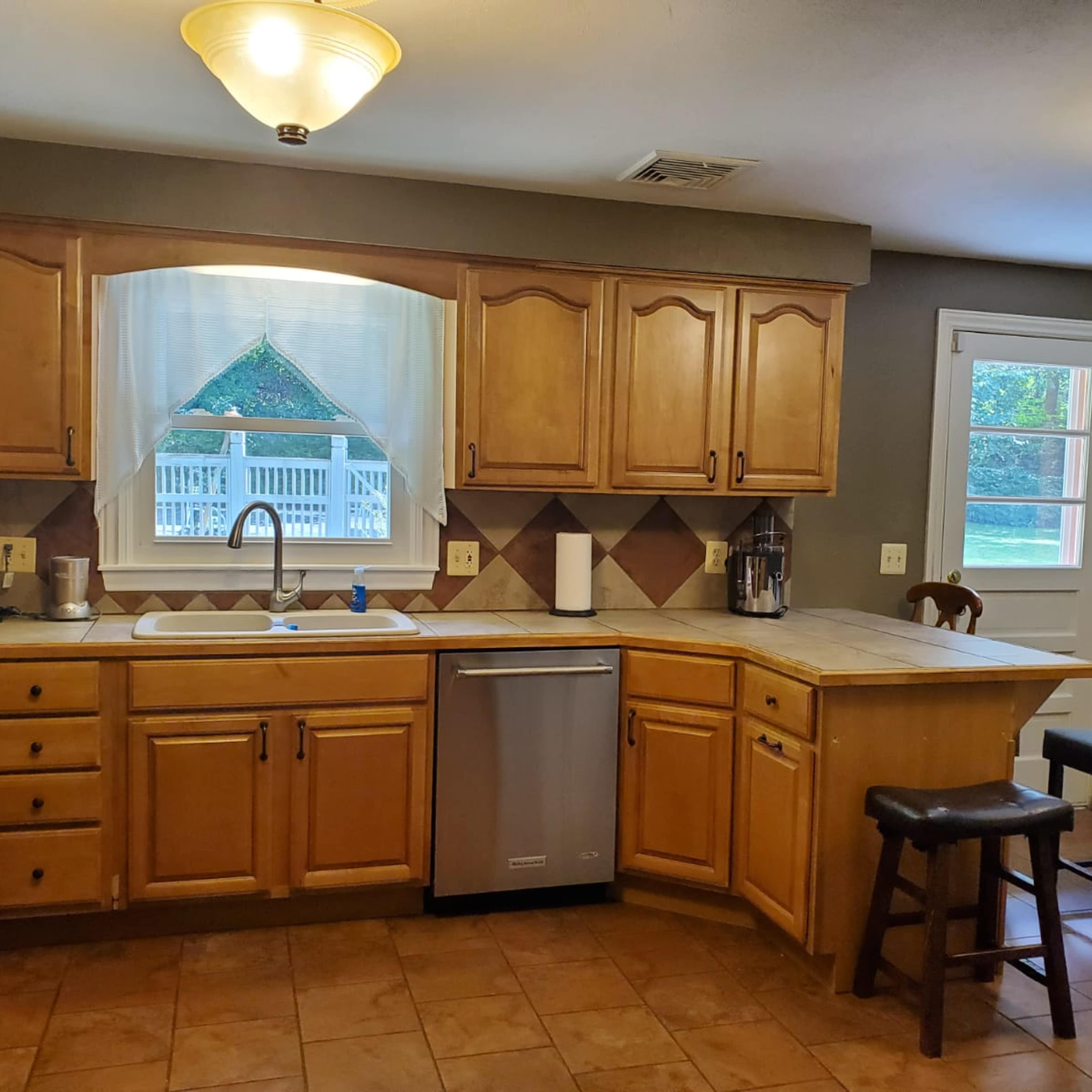 The kitchen features wooden cabinetry, a stainless steel dishwasher, and a window overlooking an outdoor deck.