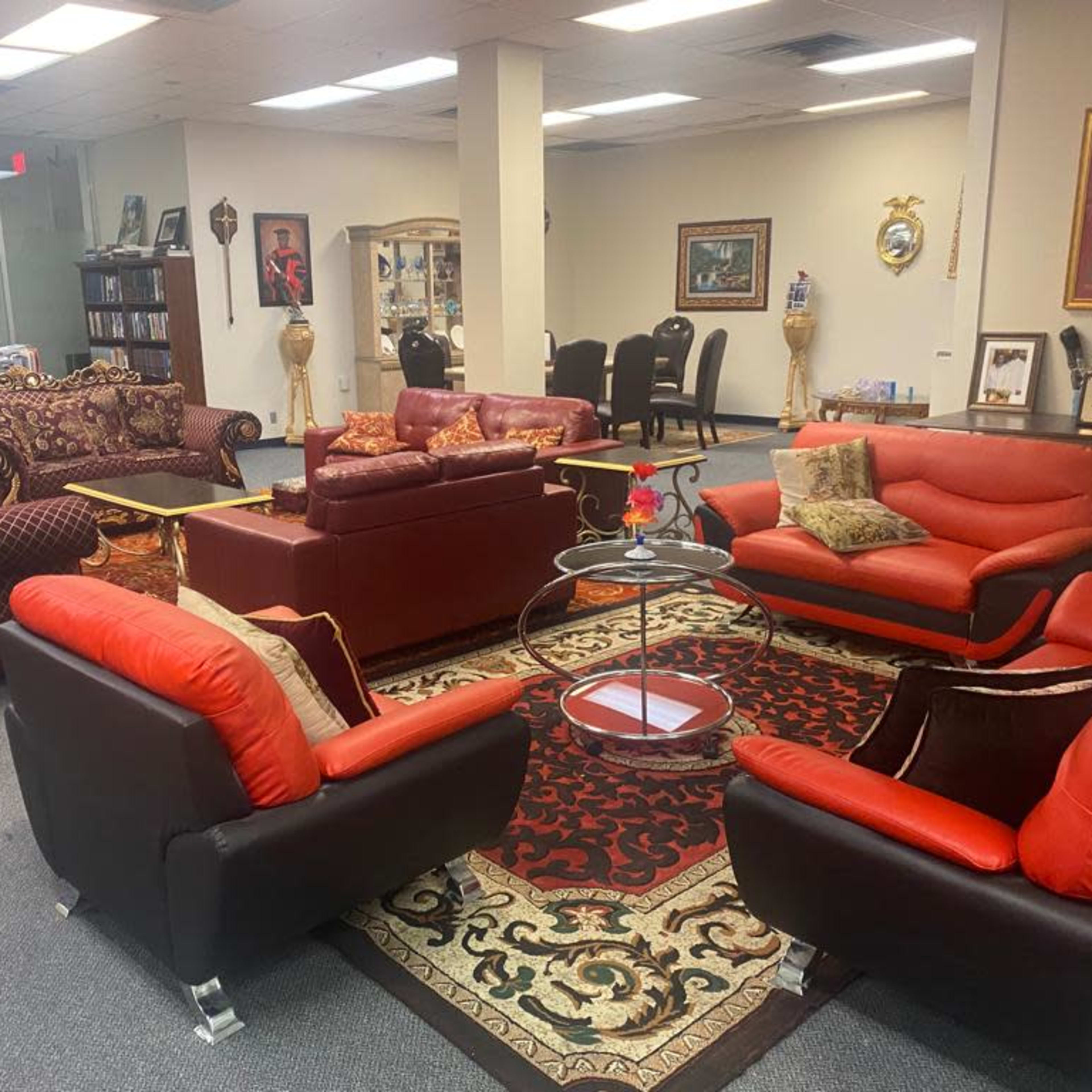 A furnished office lounge area with several seating arrangements, including red and black couches, a glass coffee table, and decorative rugs on the floor.