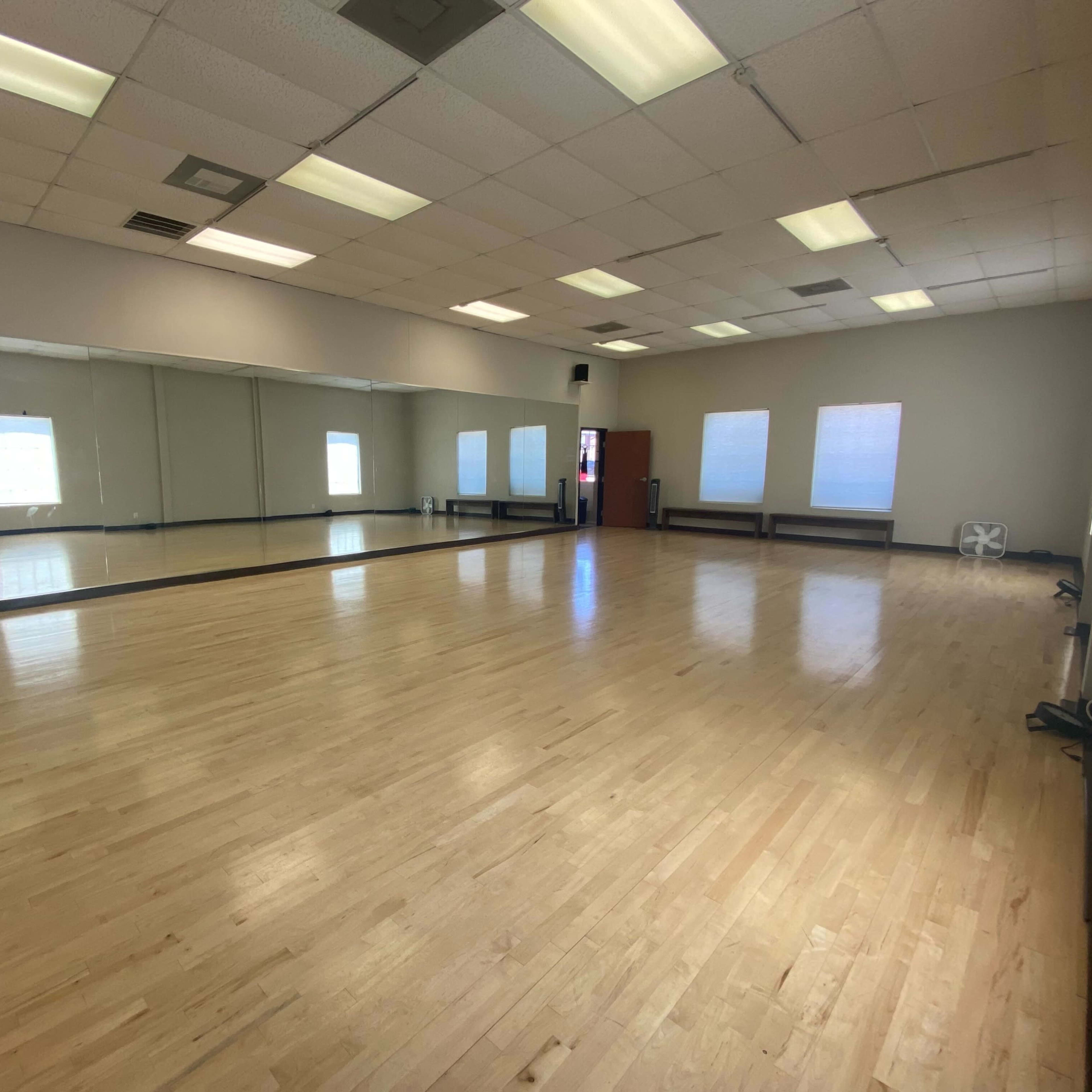 A spacious, empty dance studio with wooden flooring and large mirrors on one wall.