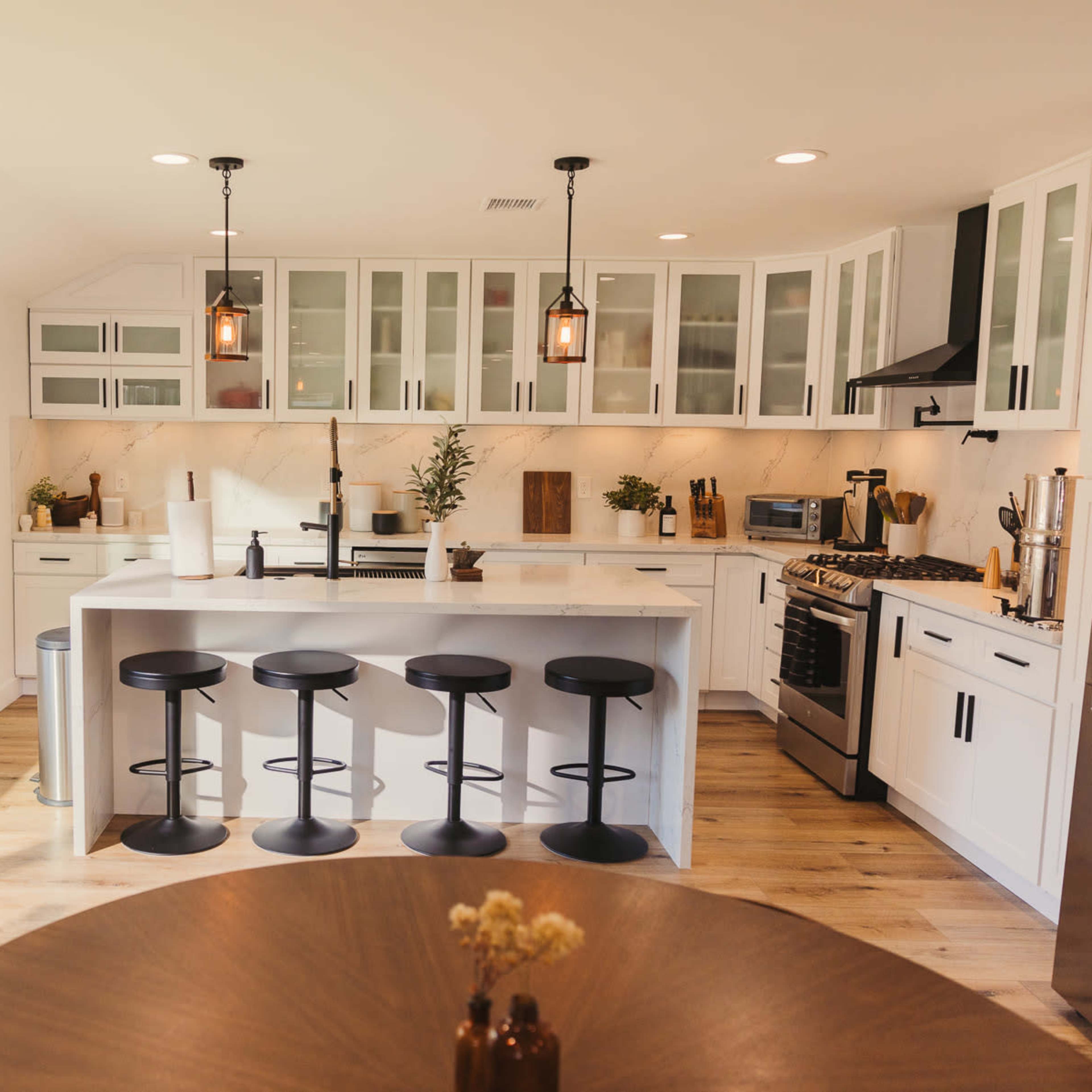 A modern kitchen with white cabinetry, a central island with black bar stools, and large windows allowing natural light.