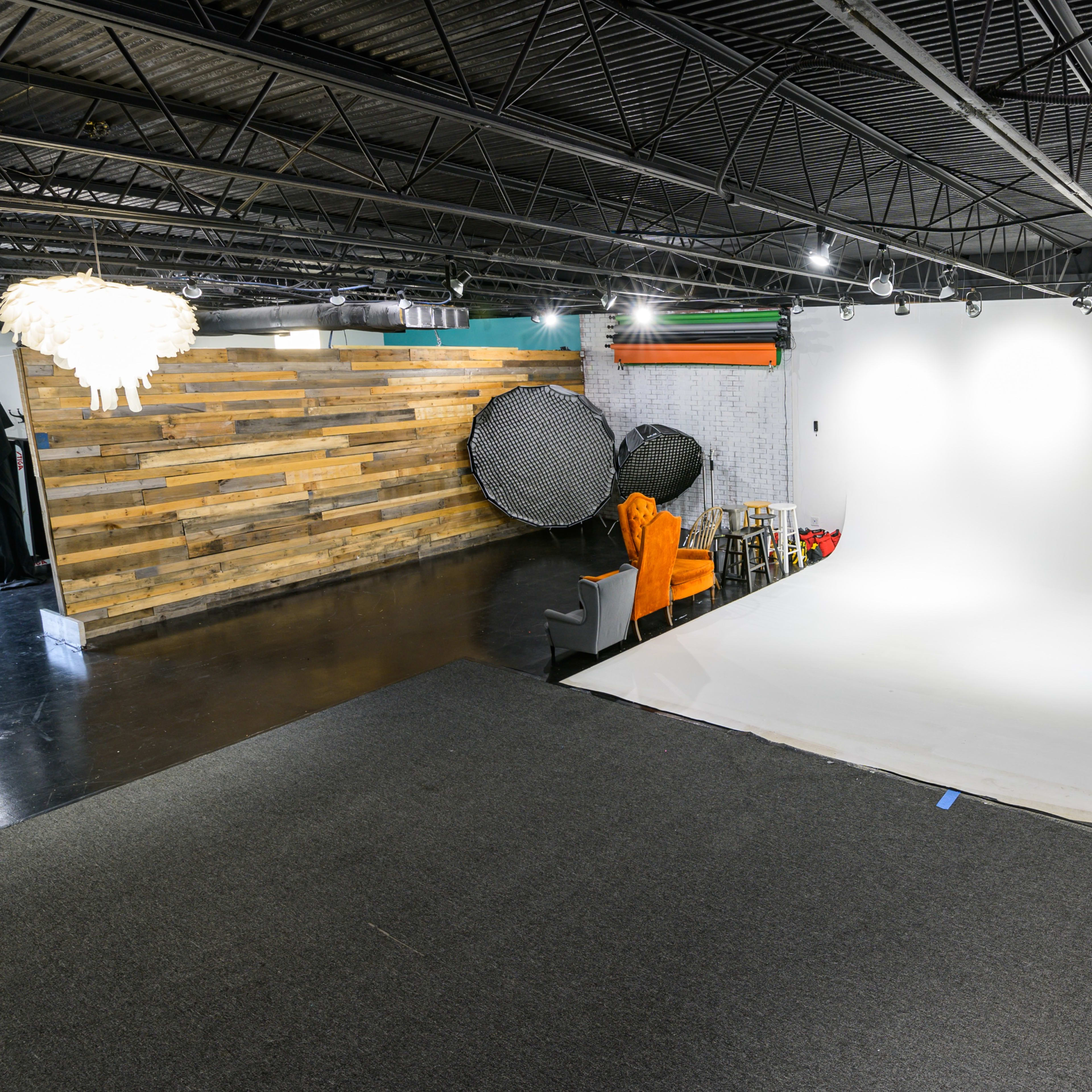 A photography studio with a seamless white backdrop, wooden accent wall, and various lighting equipment.