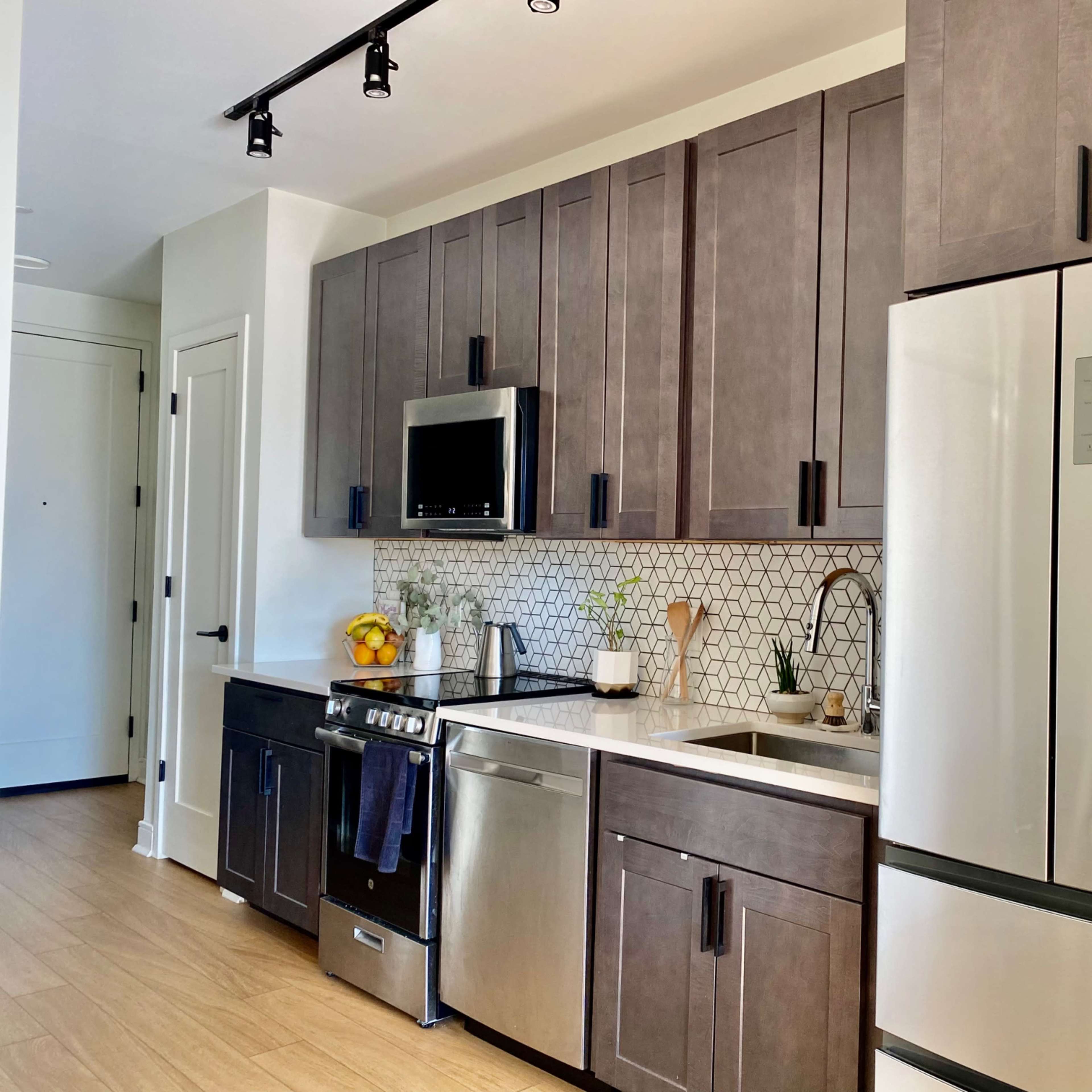 A modern kitchen with dark cabinetry, stainless steel appliances, and a tiled backsplash.