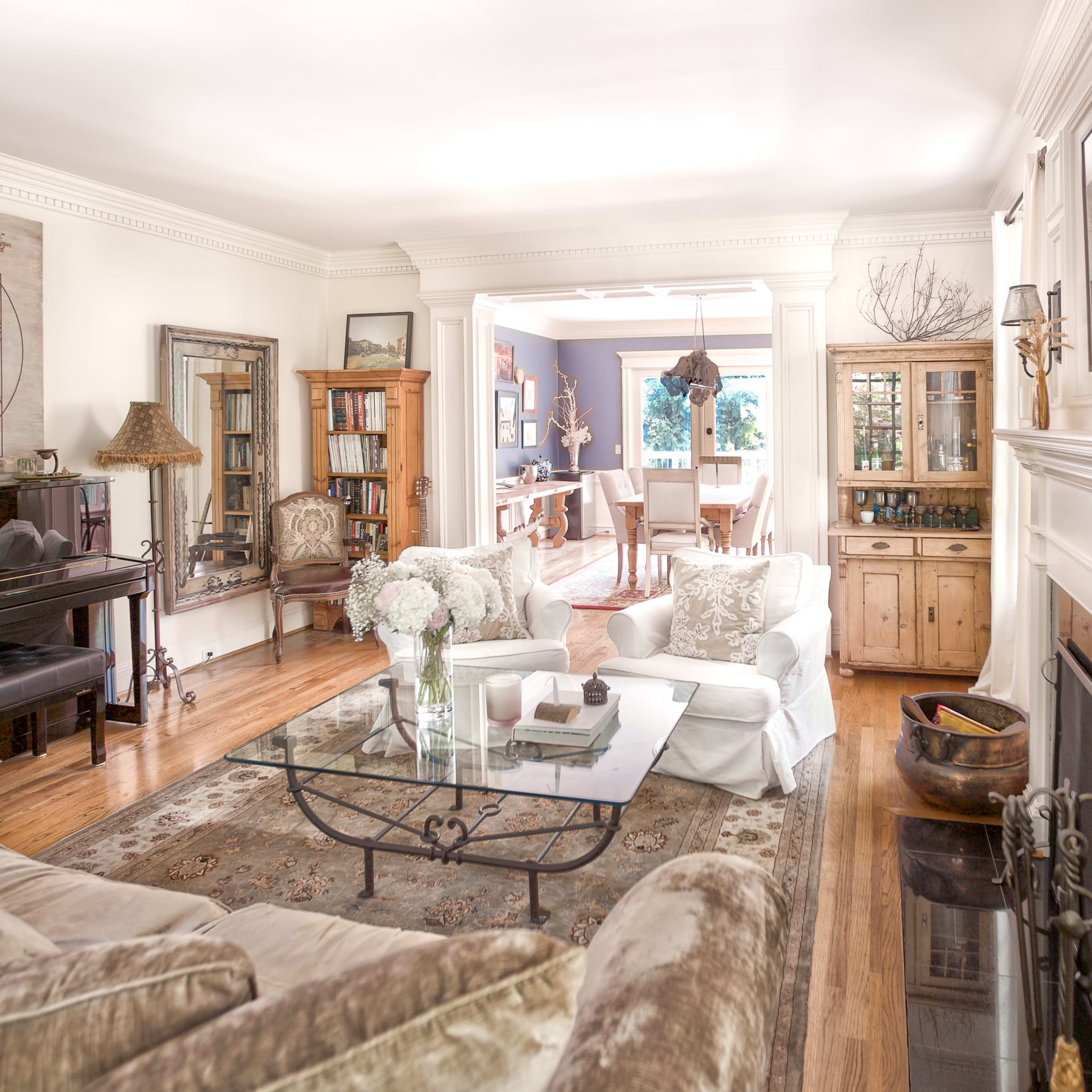 A well-lit living room with a piano, a glass coffee table, beige sofas, and a view of the dining area through an open space.
