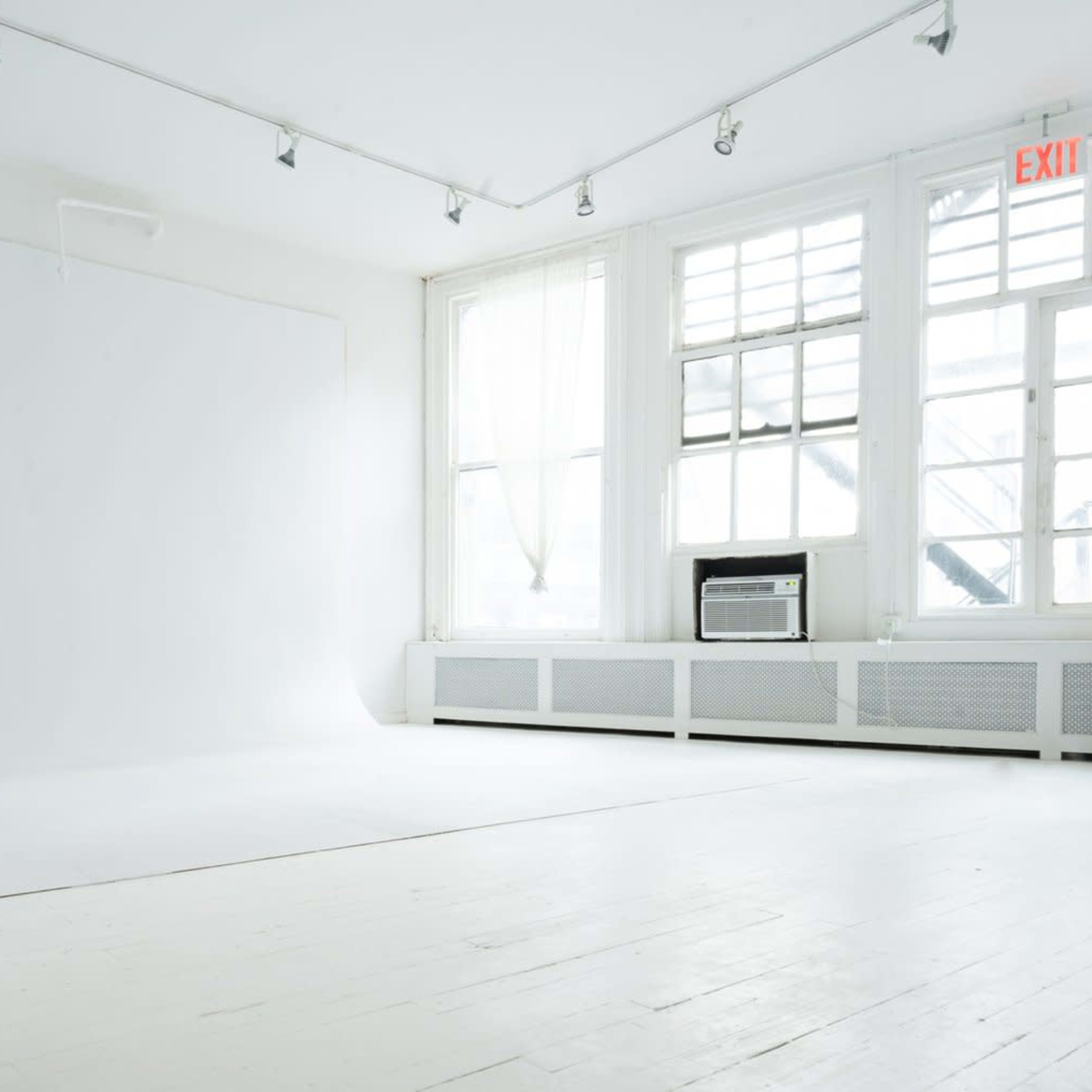 A minimalist photography studio with a seamless white backdrop and large windows allowing natural light to enter.