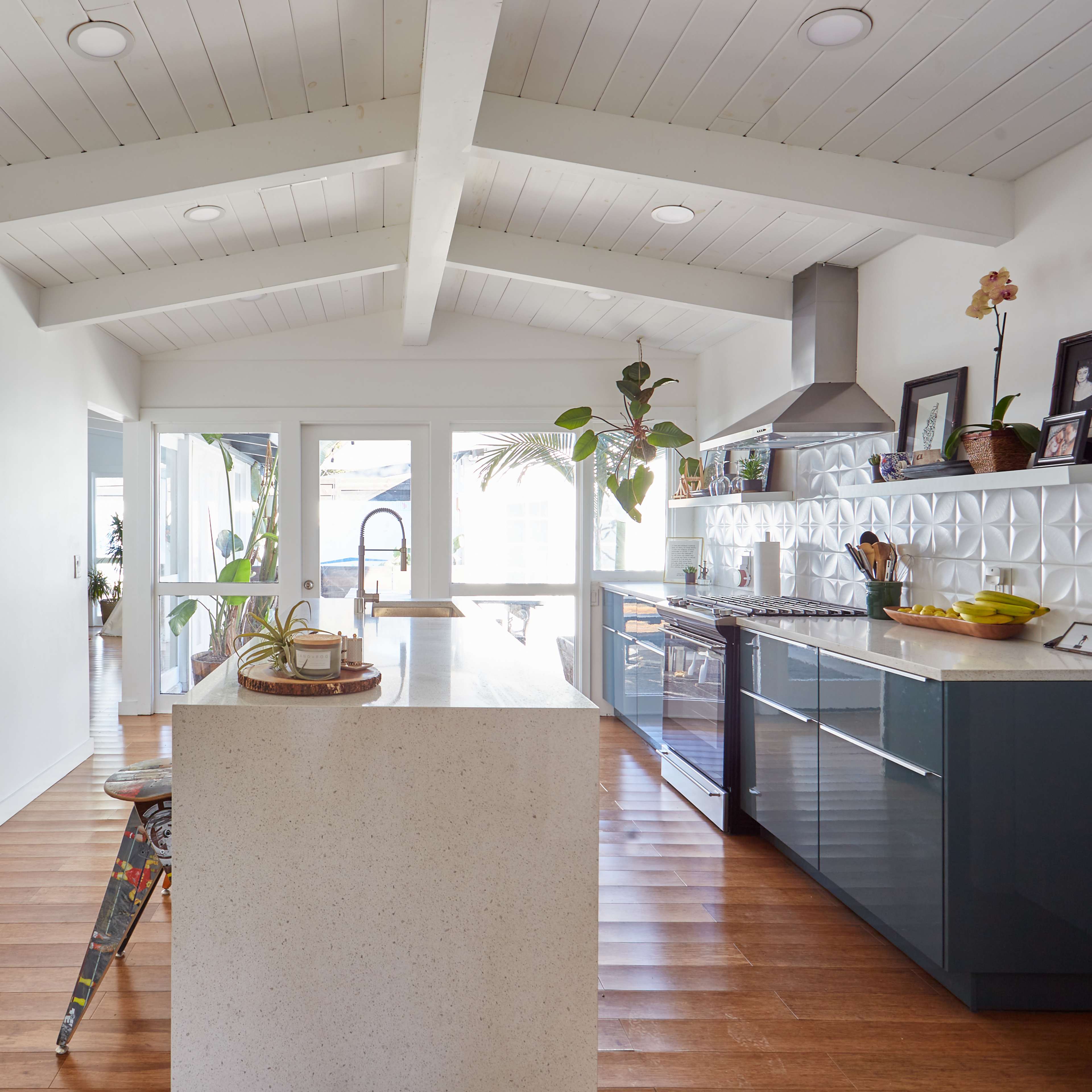 A modern kitchen with a central island, flat-panel cabinets, and a stainless steel range hood beneath a vaulted ceiling.
