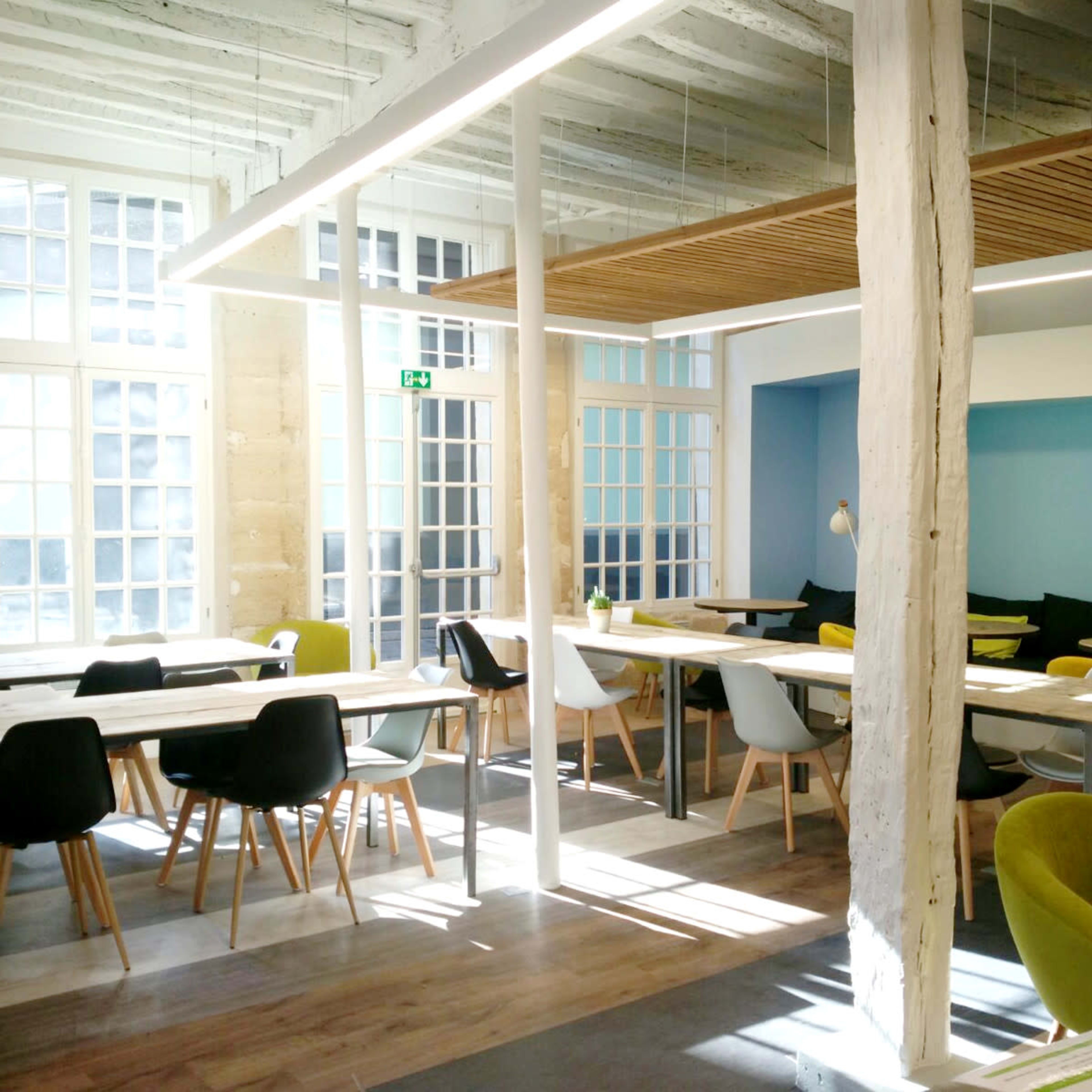 A modern, airy café with various seating arrangements, large windows, and colorful accent walls.