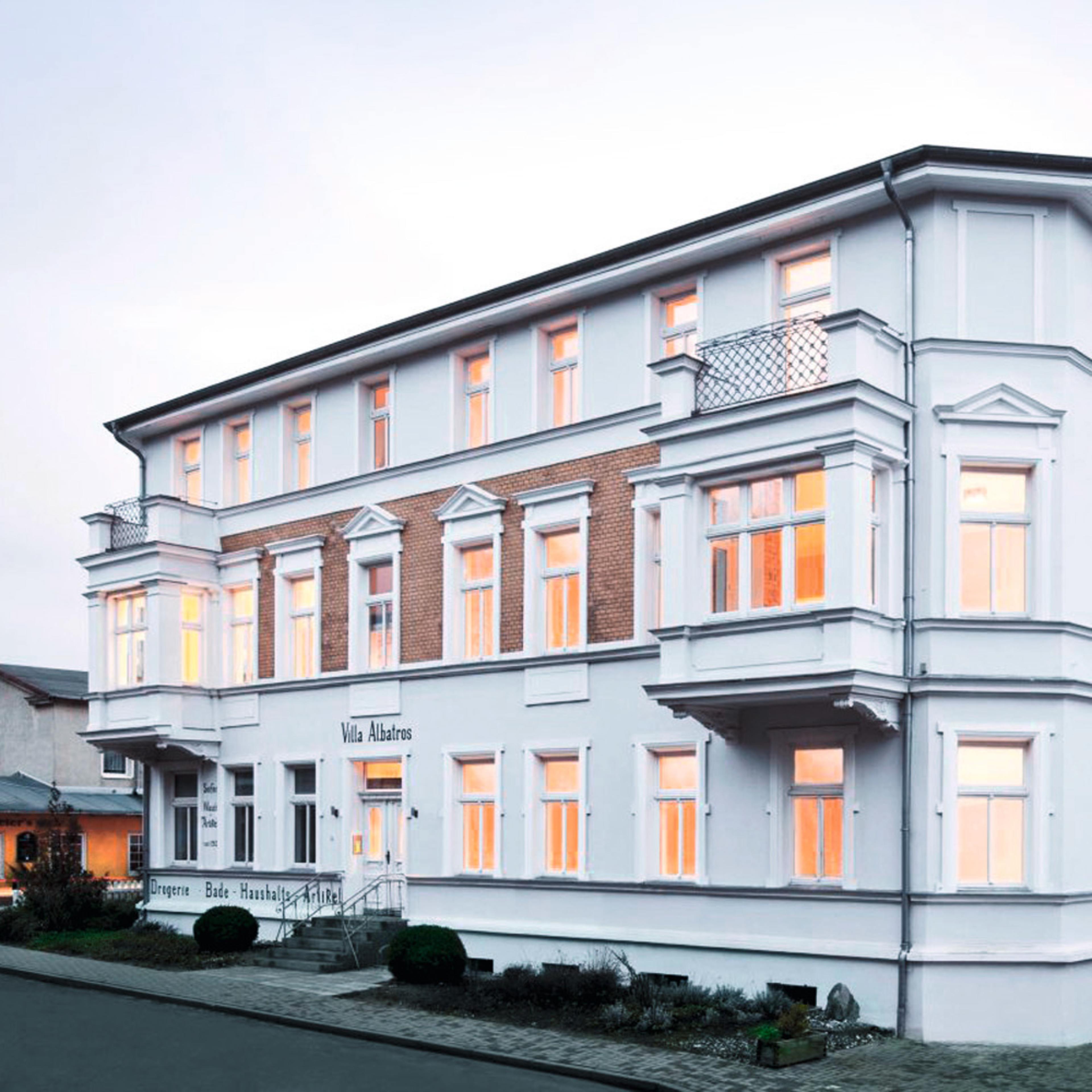 A three-story white building with numerous windows is located on a street, featuring a classic architectural design.