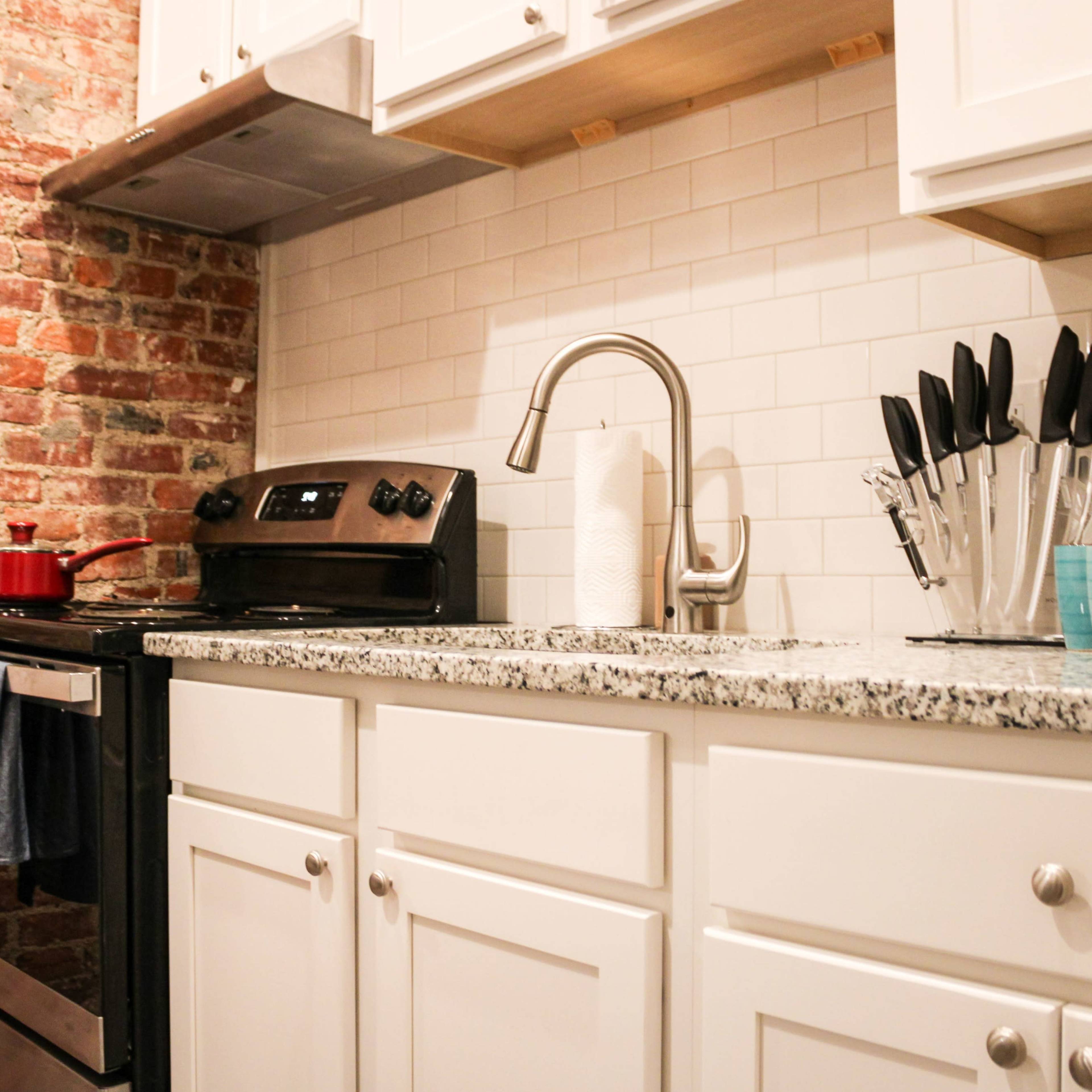 A kitchen featuring exposed brick walls, a stainless steel stove, and a countertop with various kitchen utensils arranged in a holder.