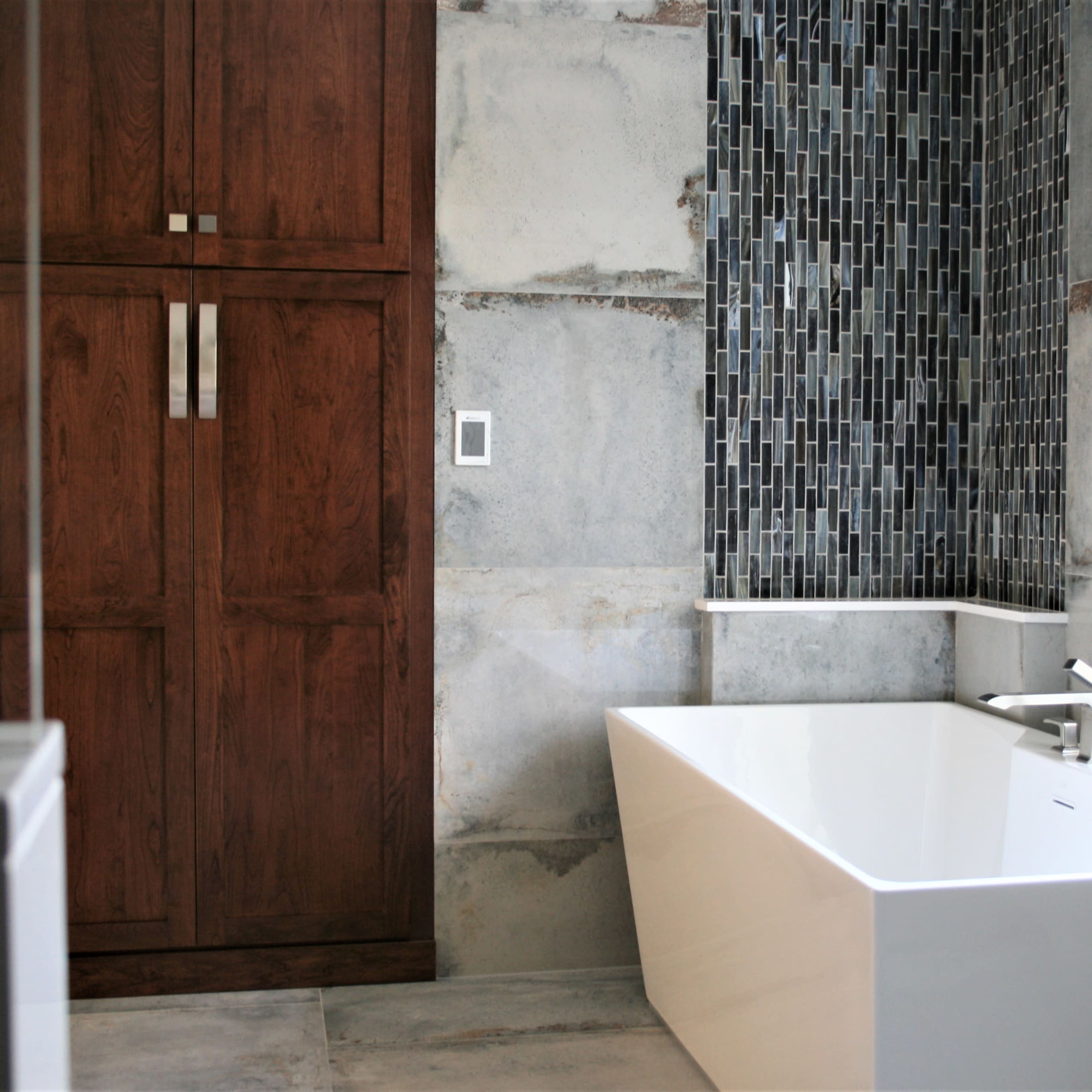 A modern bathroom featuring a freestanding white bathtub, dark wooden cabinetry, and a textured tiled wall.
