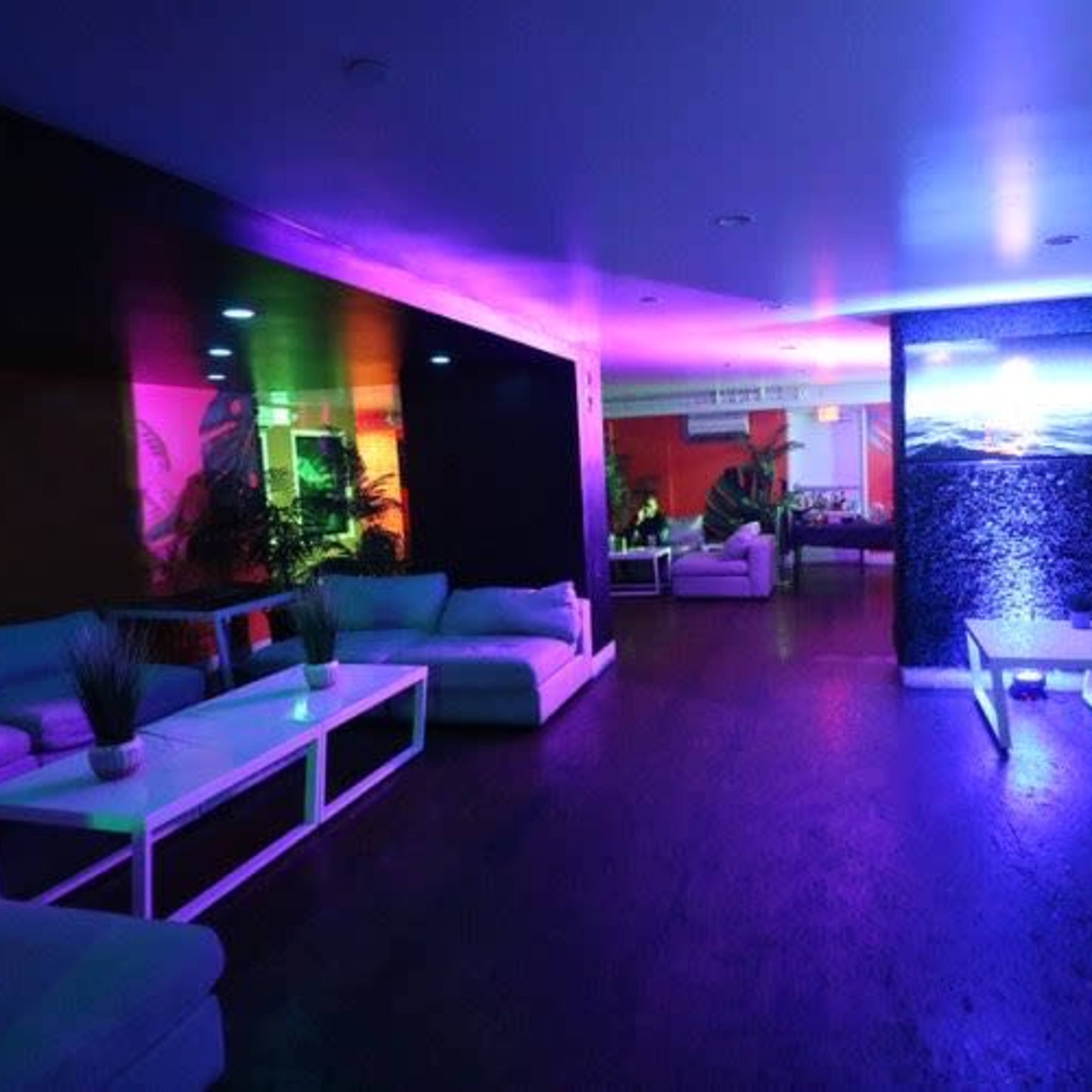 A lounge area features white couches and a large screen, illuminated by colorful lights.