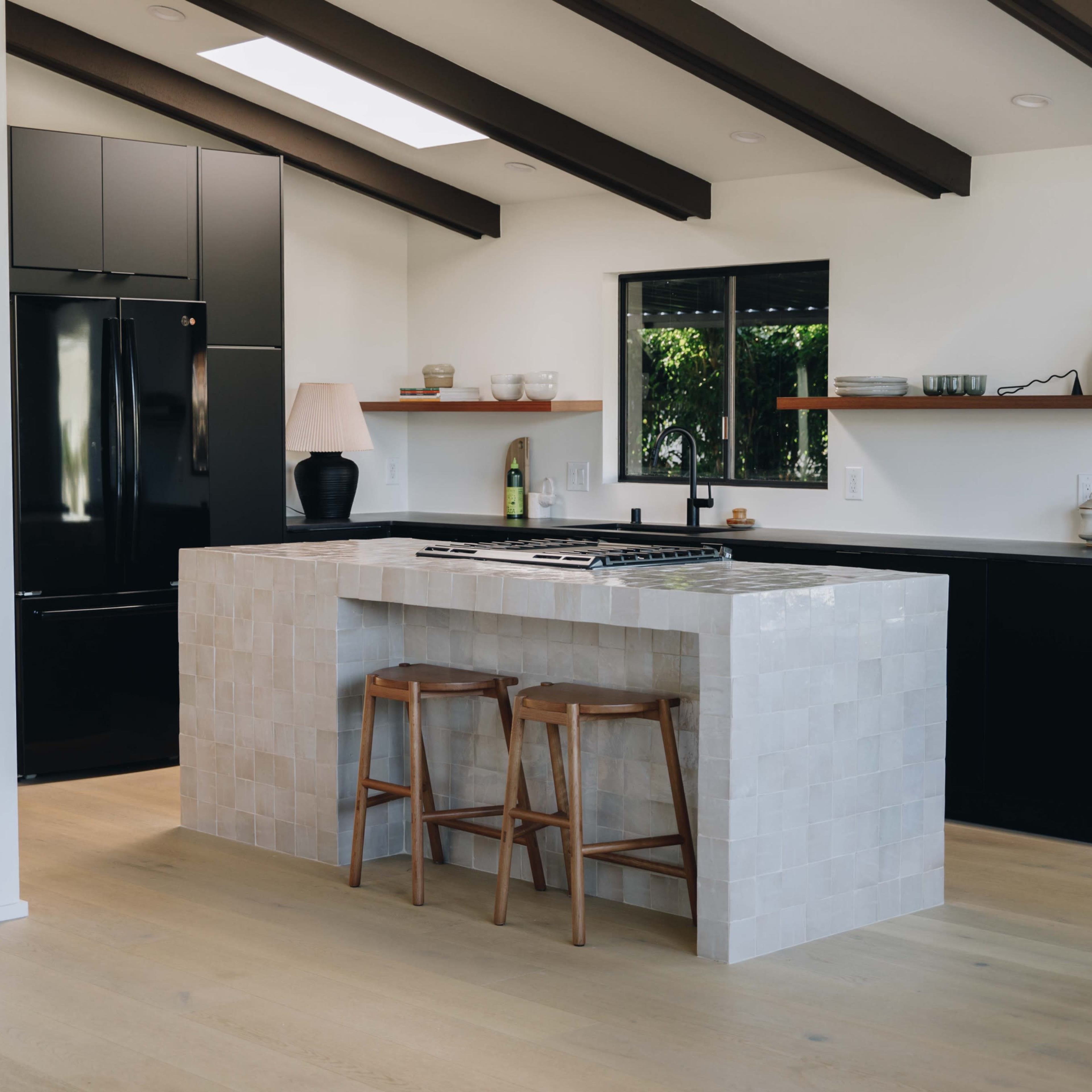 A modern kitchen features a central island with a stovetop, black appliances, and light wood flooring.
