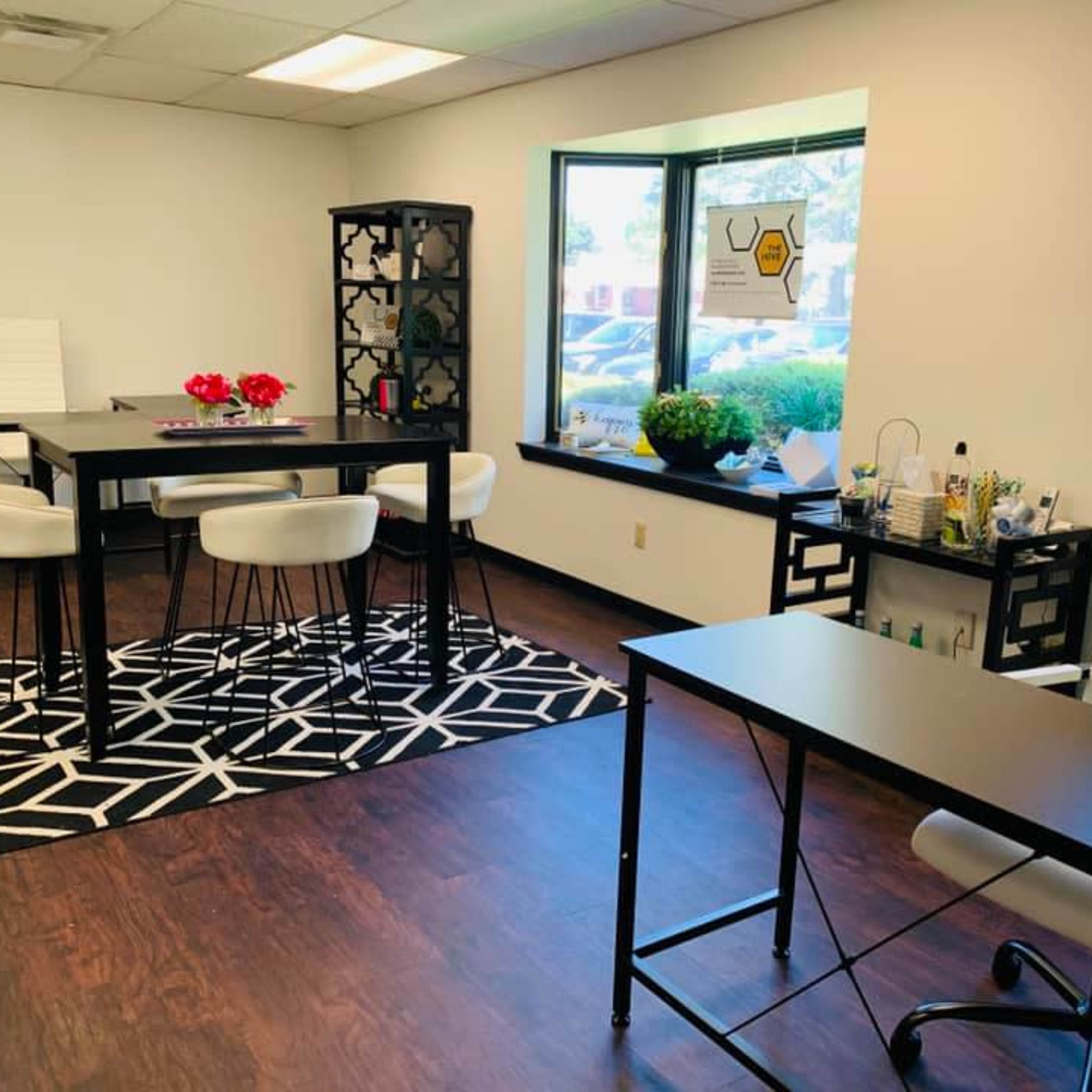 A modern office space with two black desks, white chairs, a patterned rug, and a large window letting in natural light.