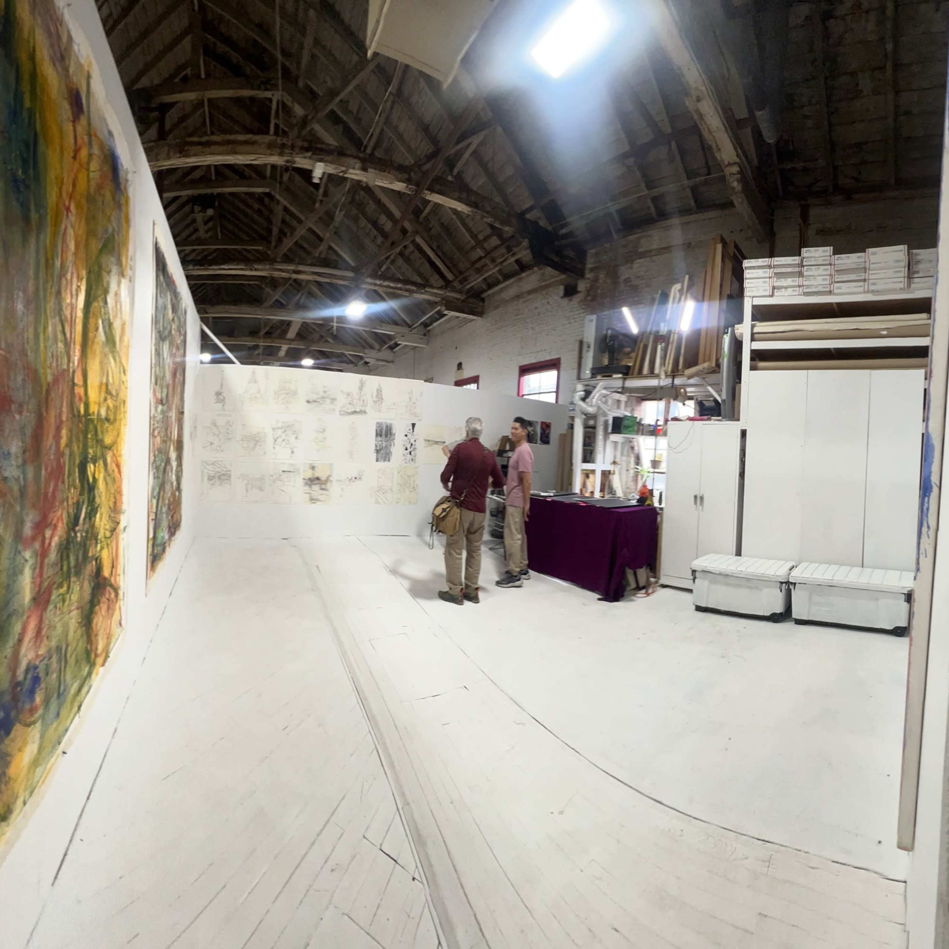 An artist is positioned near a large abstract painting in a spacious gallery with exposed wooden beams.