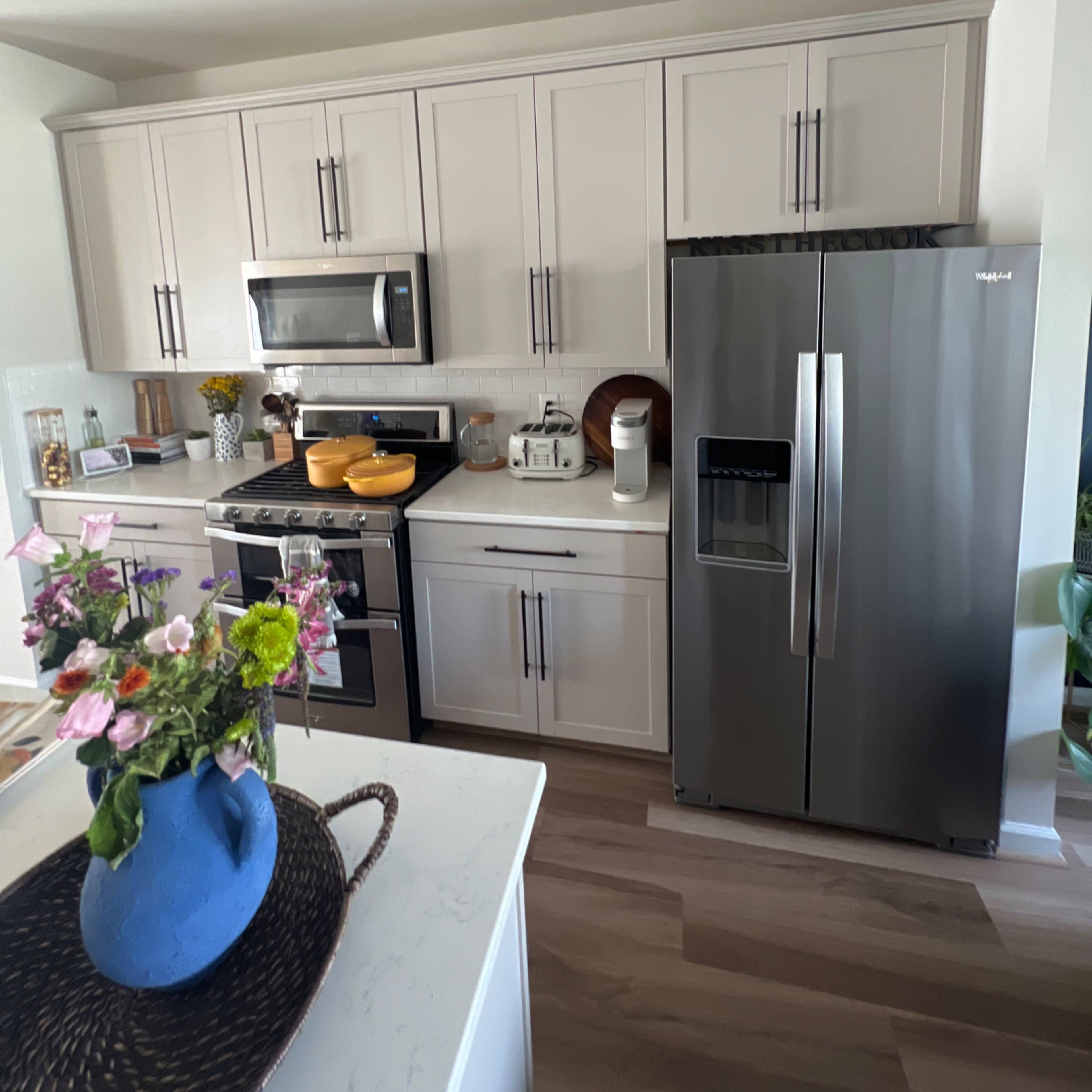 The kitchen features modern cabinetry, stainless steel appliances, and a countertop with decorative items and a blue vase containing flowers.
