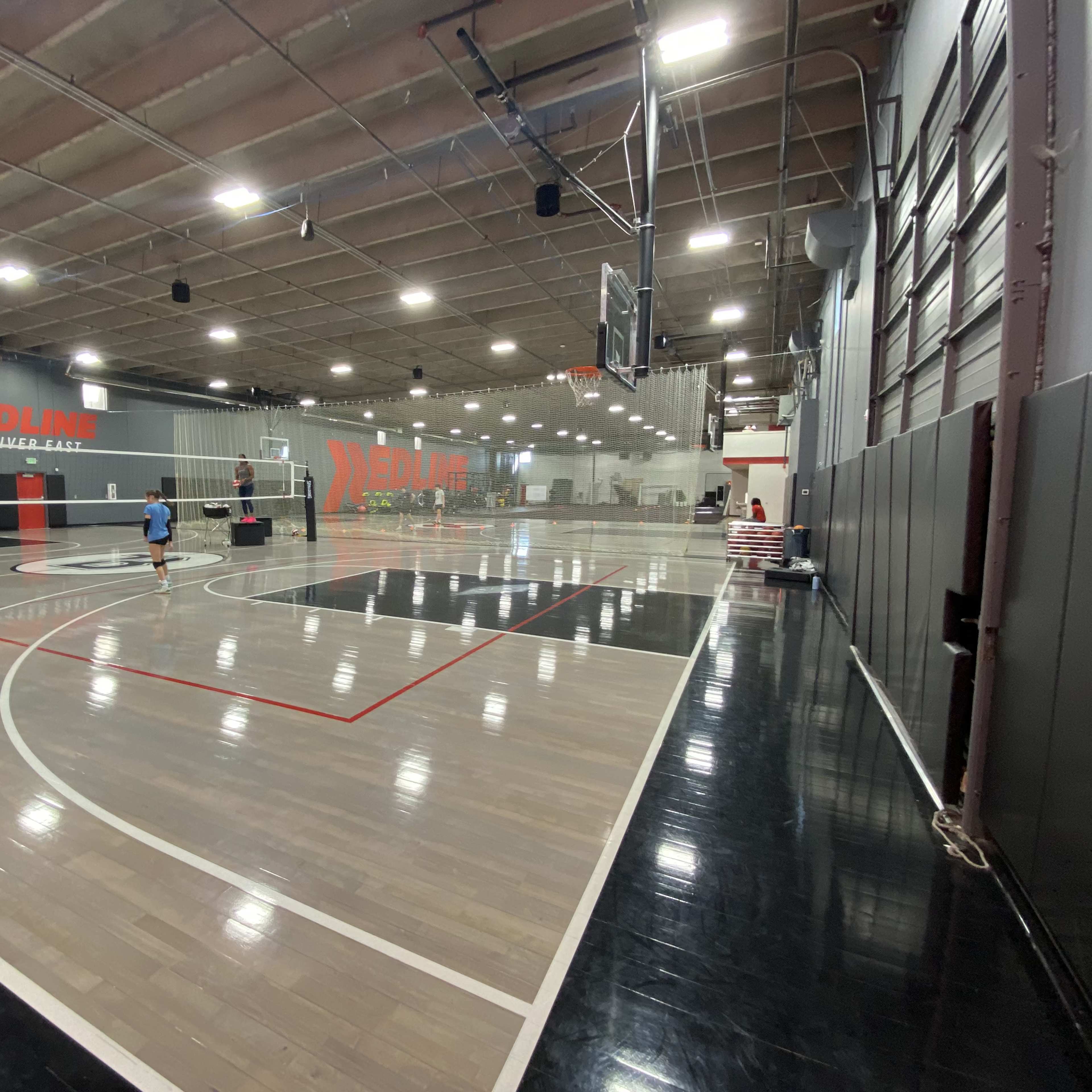 A spacious indoor sports facility with a basketball court on one side and a volleyball court on the other.