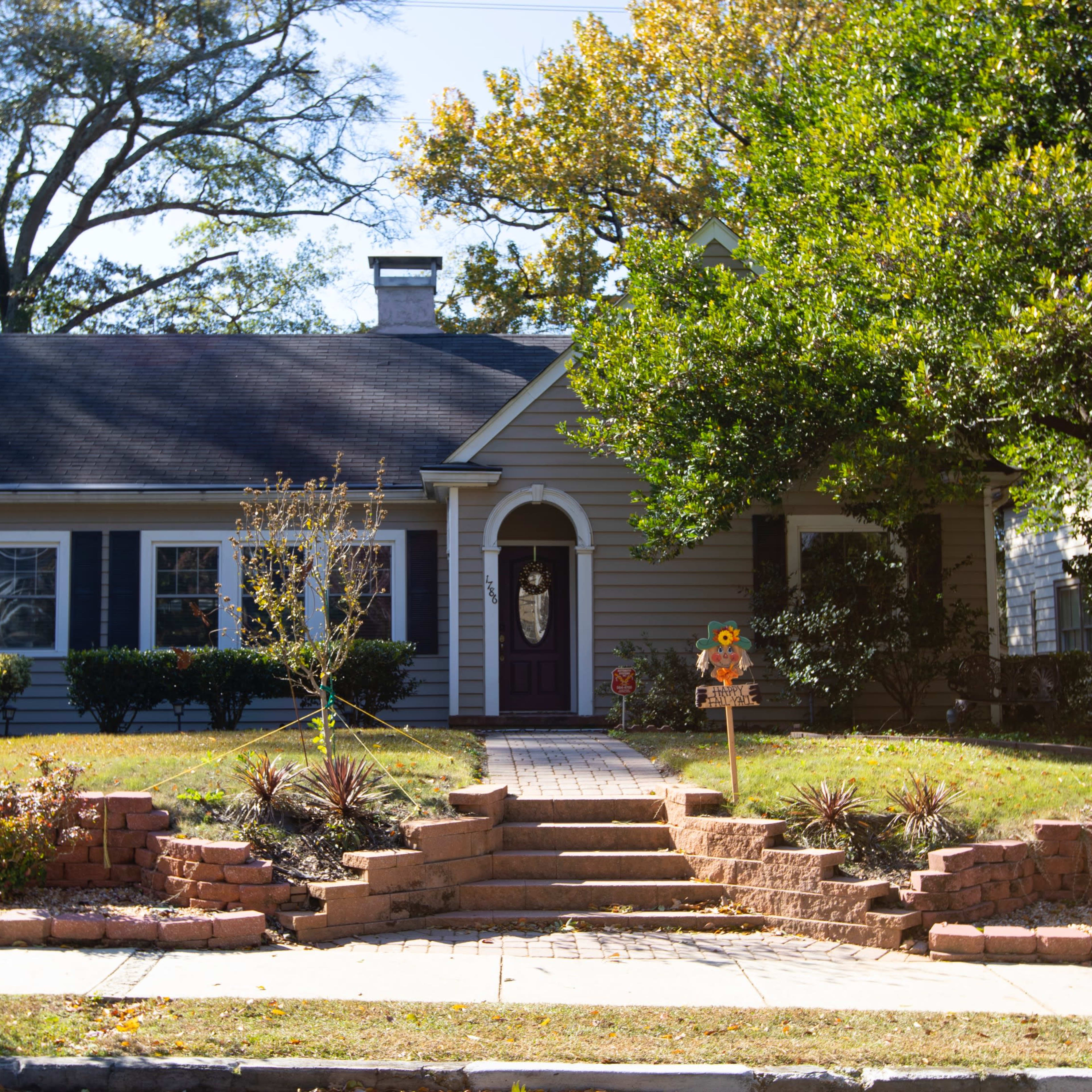A single-story, gray house with a purple door features a landscaped front yard and a brick pathway leading to the entrance.