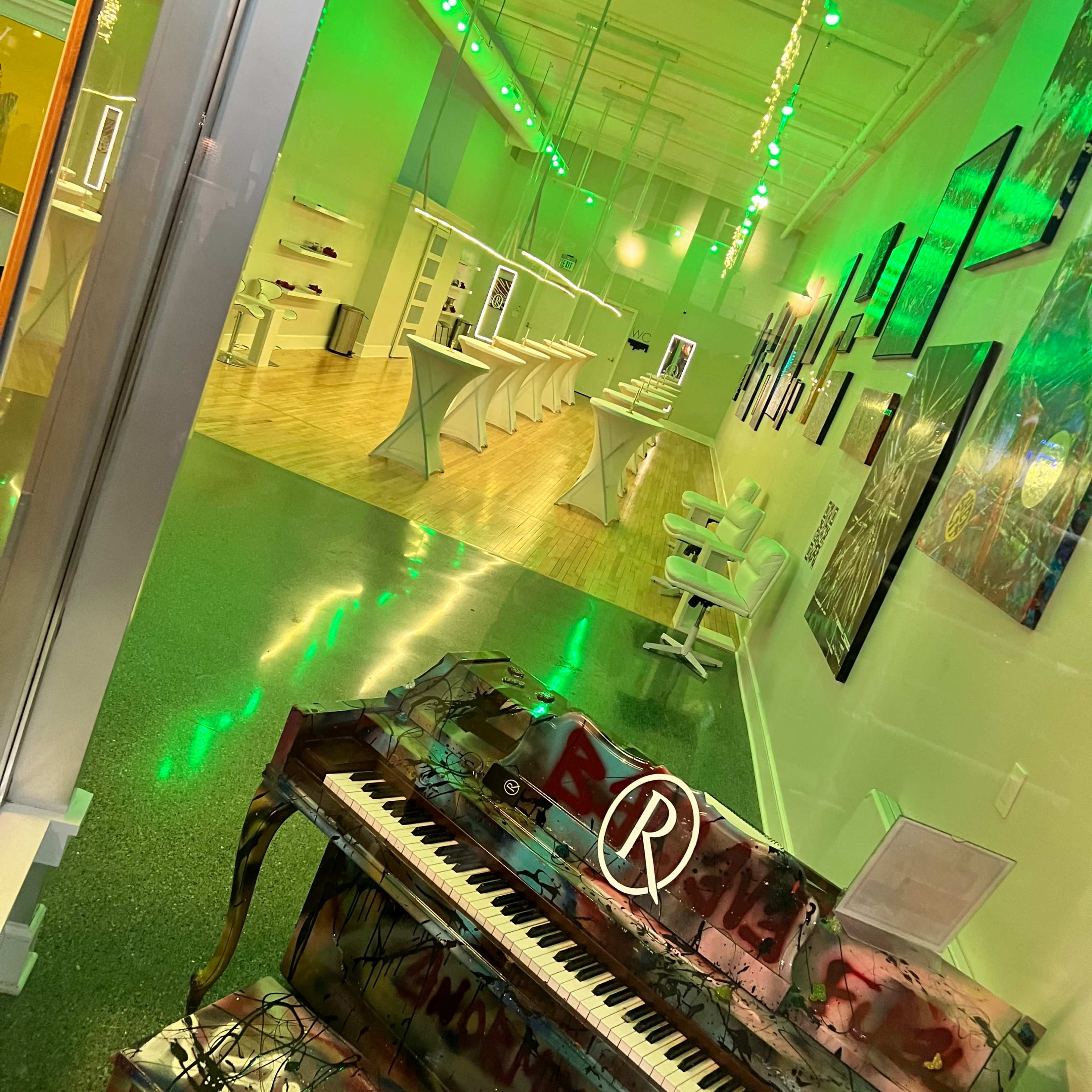 A brightly lit modern interior space featuring a colorful grand piano in the foreground and white furniture arranged along the walls.