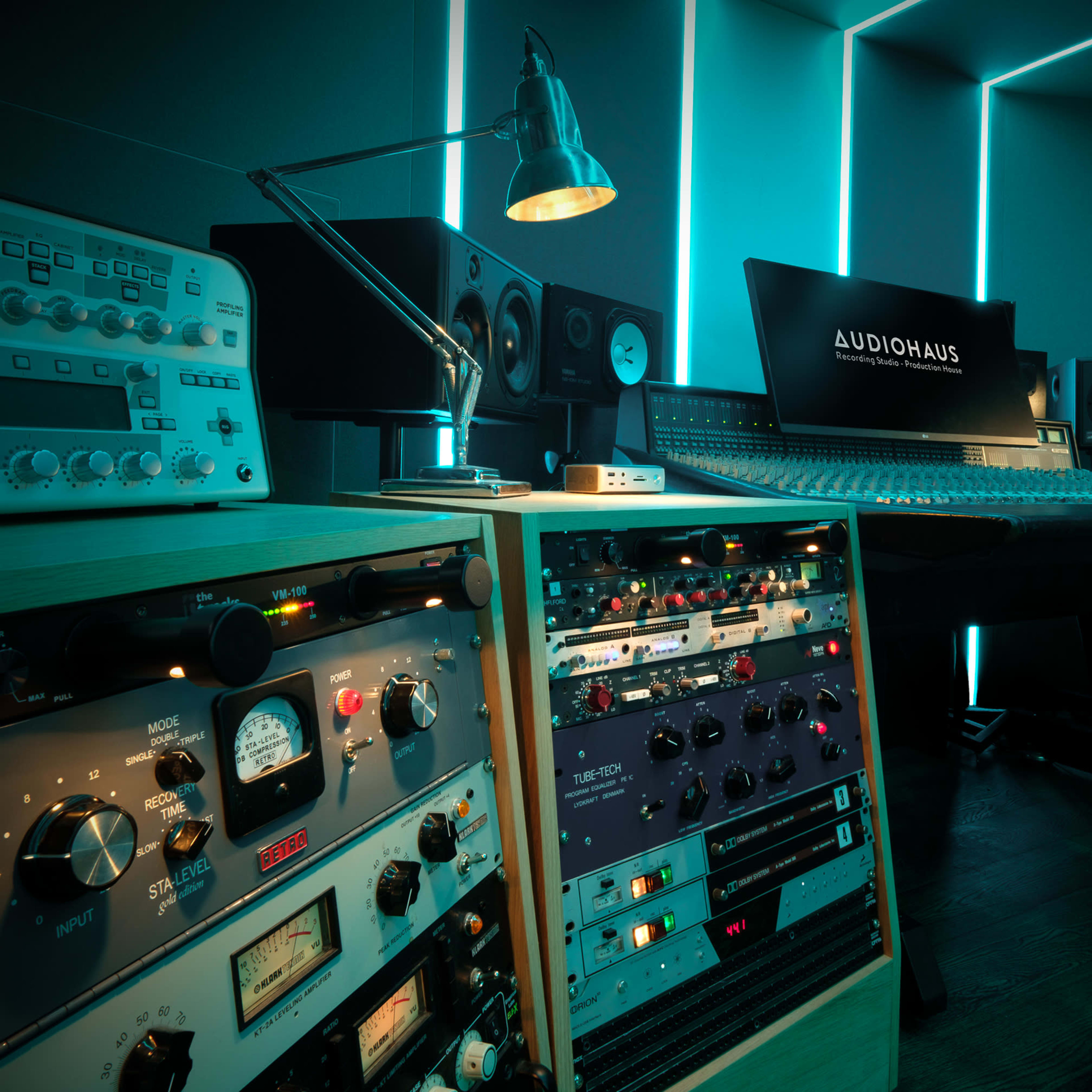 A modern audio recording studio with a central mixing console, rack-mounted equipment, and ambient lighting.