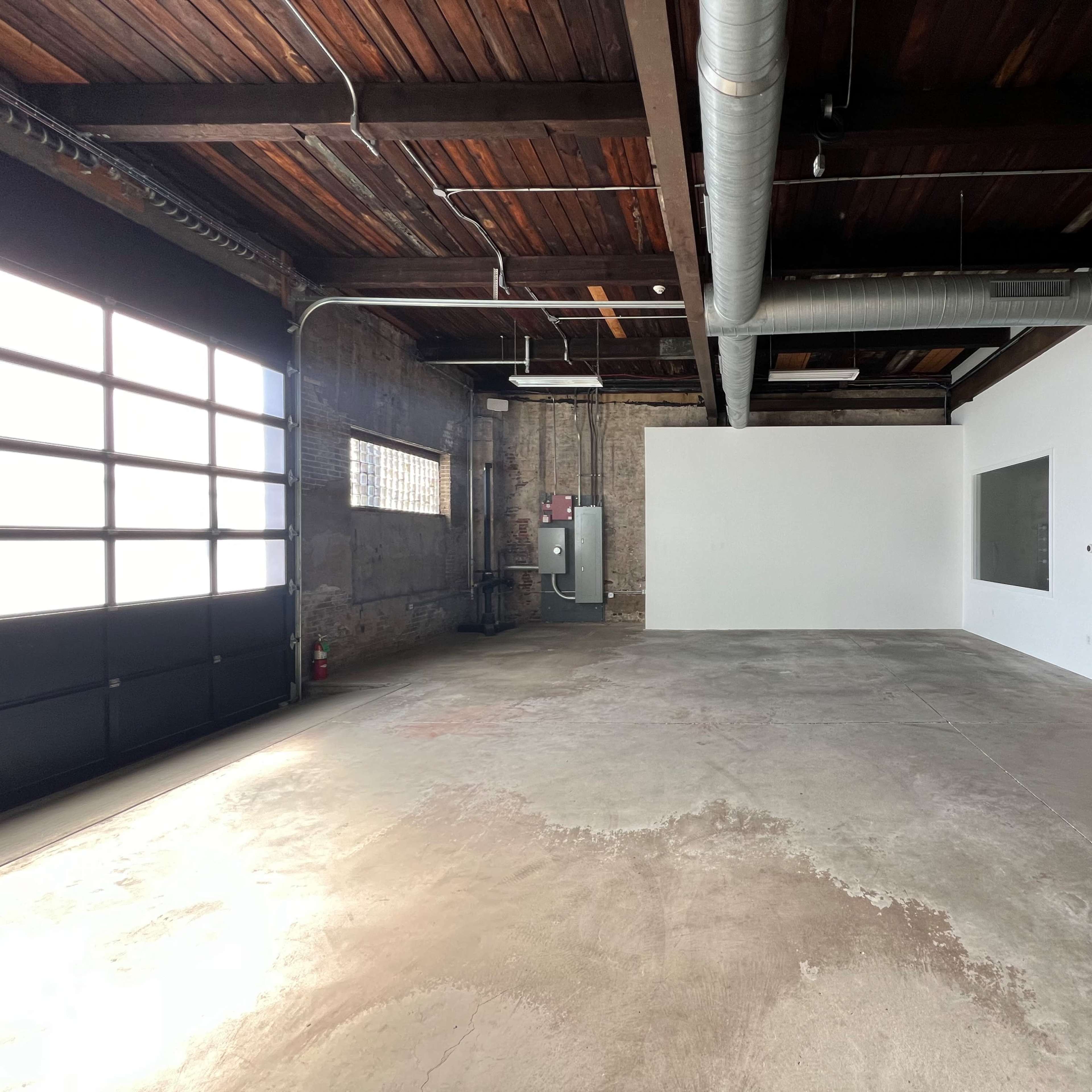 A spacious, empty industrial-style room with exposed wooden beams, a concrete floor, and large windows.