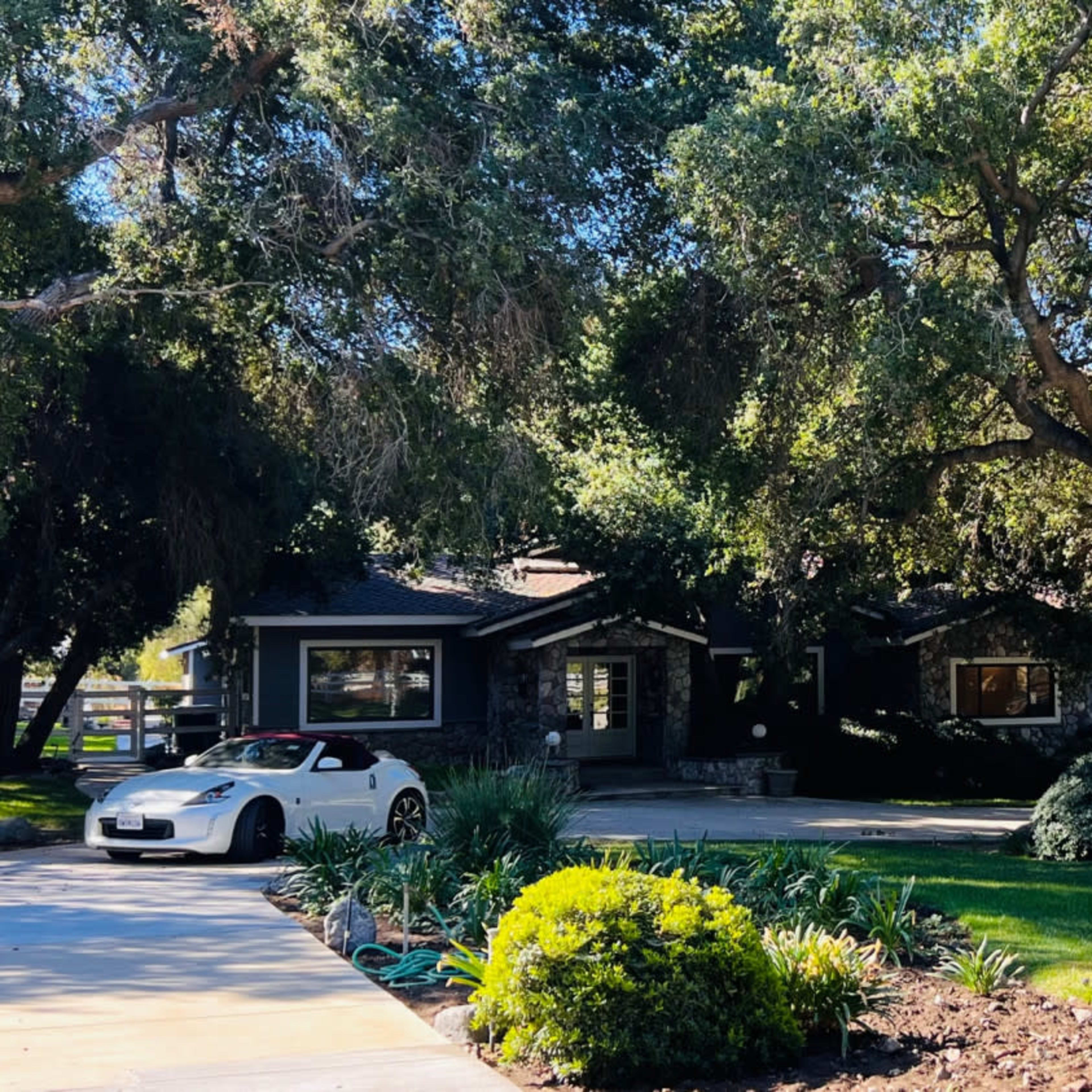 A modern house with a stone facade is surrounded by large trees and manicured lawns.
