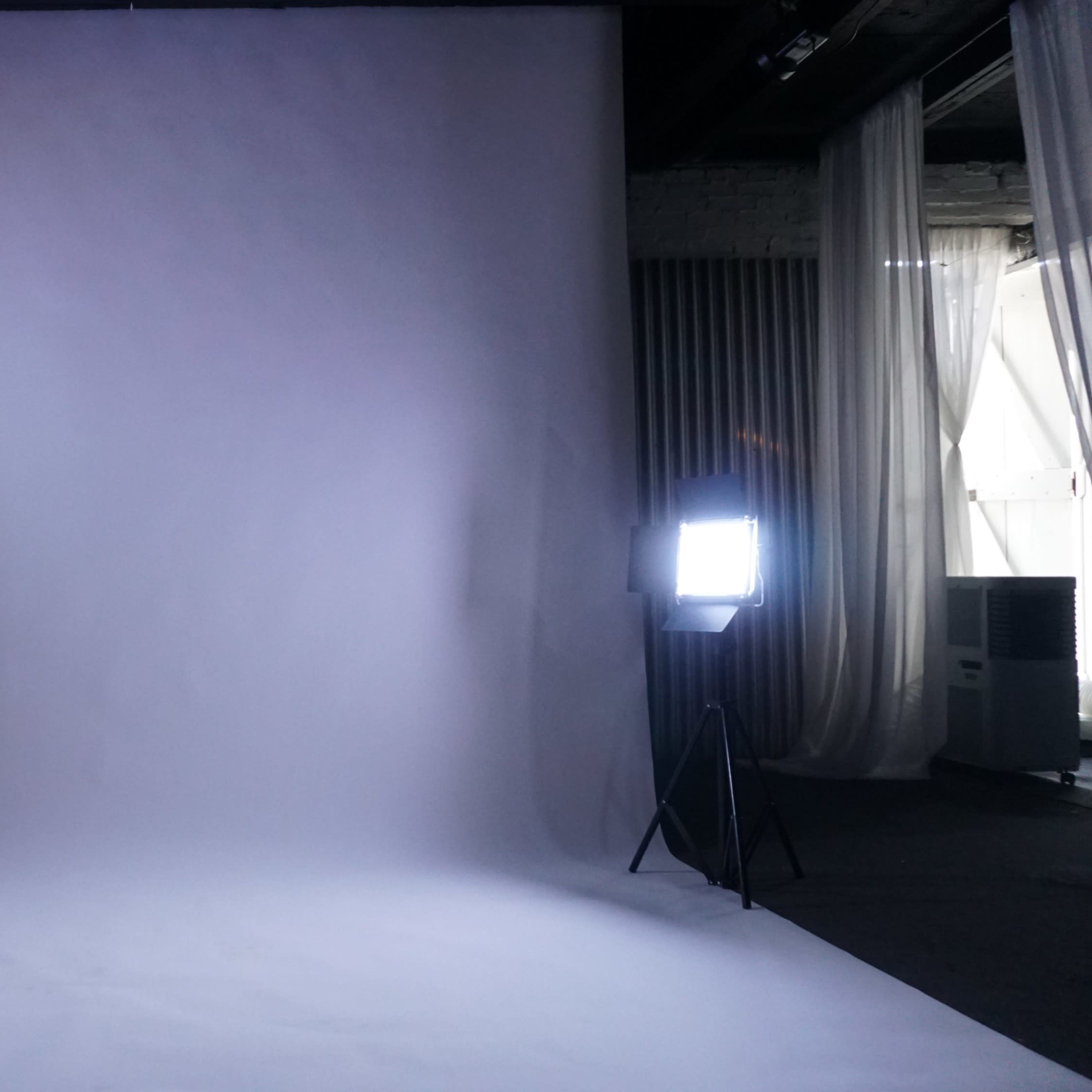A photography studio with a plain backdrop and two lighting fixtures on either side.