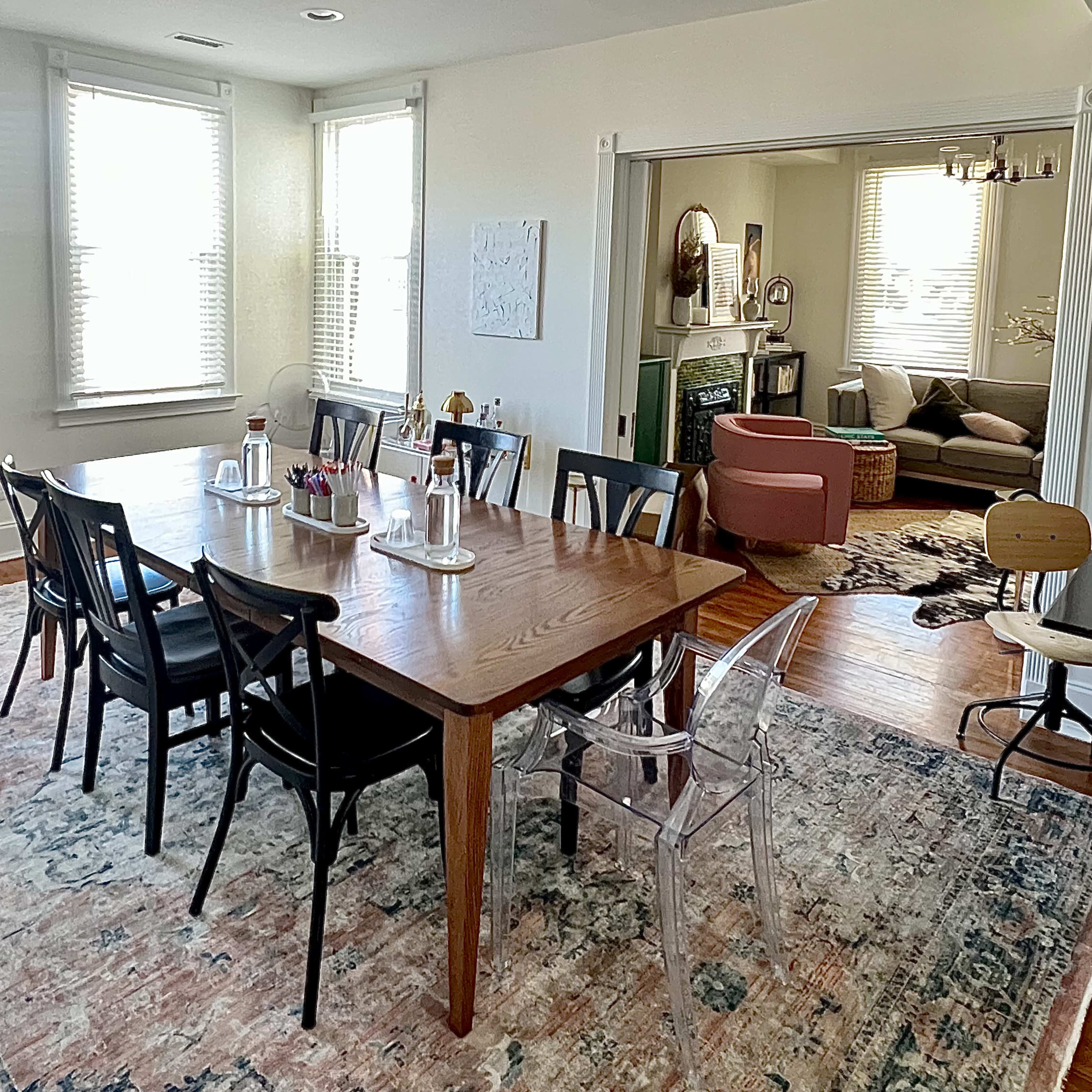 A dining area with a large wooden table surrounded by black chairs, adjacent to a living room with a couch and decorative elements.