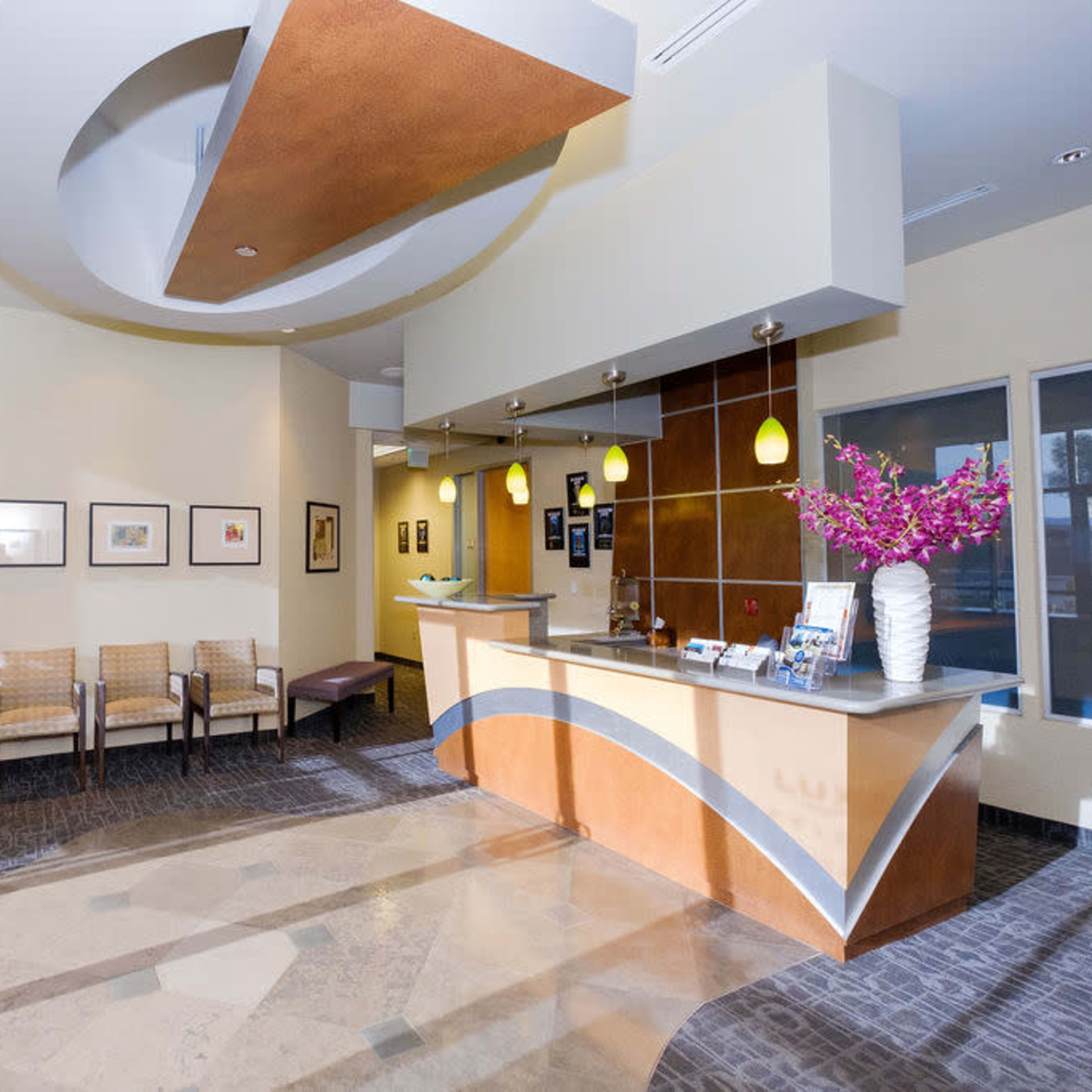 A modern reception area with a curvy front desk, comfortable seating, and decorative plants under bright lighting.