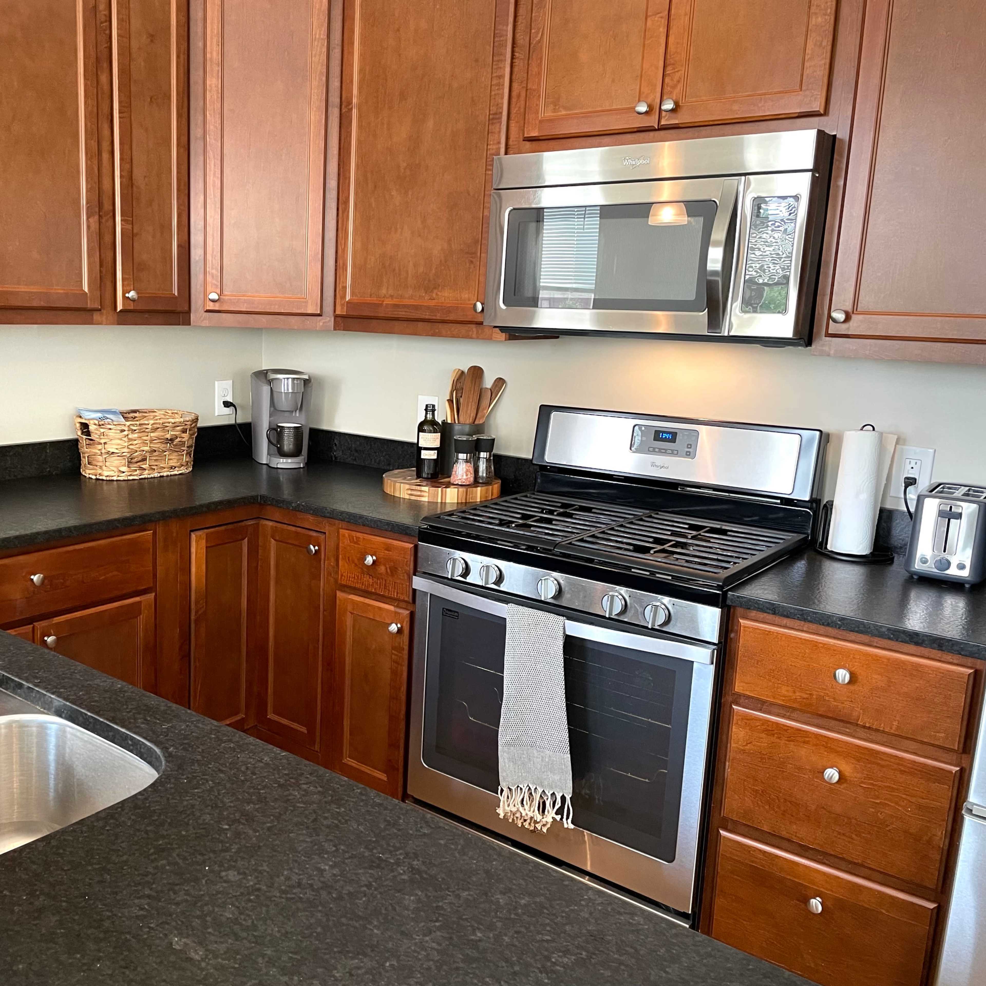 A modern kitchen features wooden cabinets, stainless steel appliances, and a black countertop with a sink and various utensils.