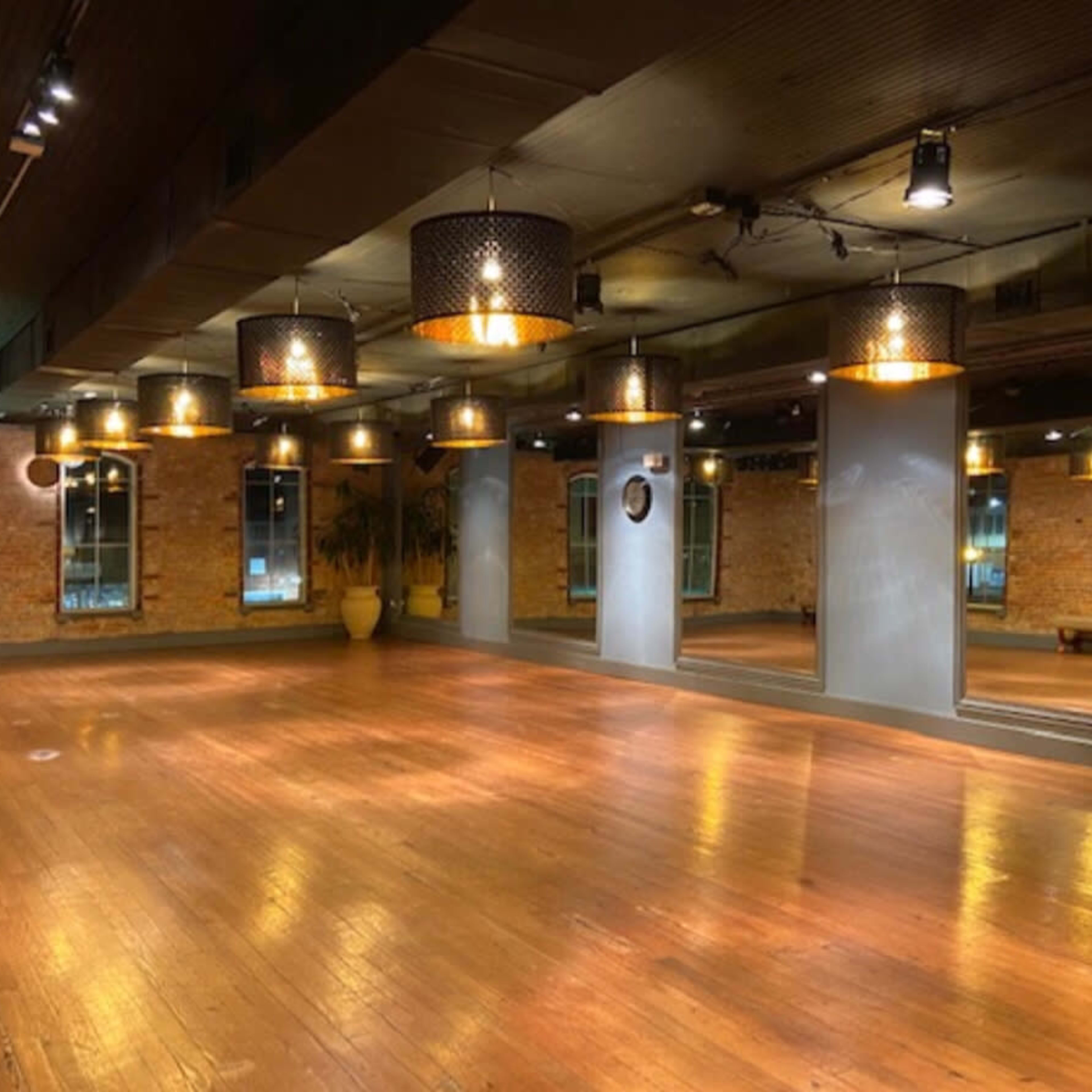 An empty interior space with wooden floors, exposed brick walls, and pendant lighting.
