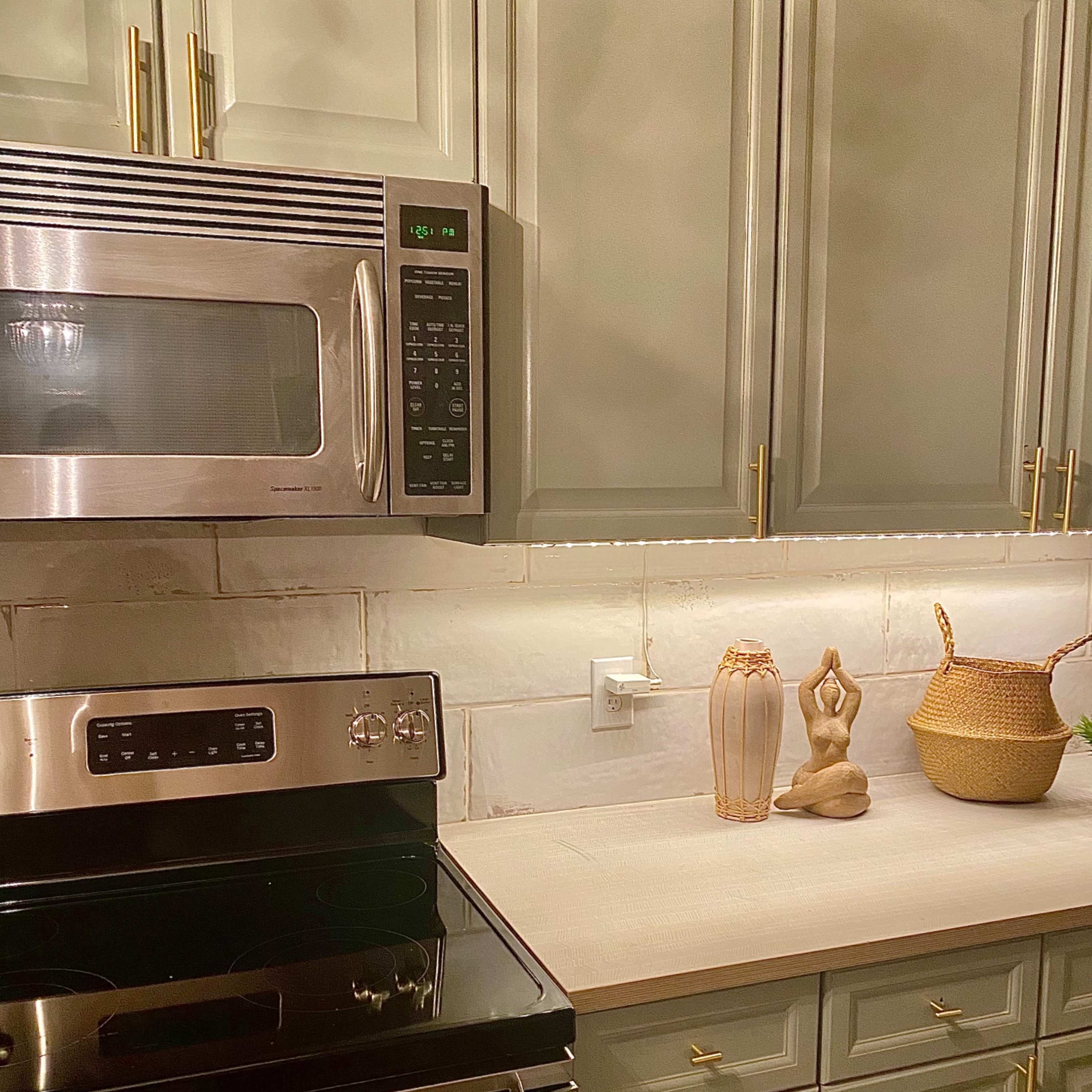 A kitchen featuring stainless steel appliances, gray cabinetry, and a countertop decorated with a wooden sculpture and woven basket.