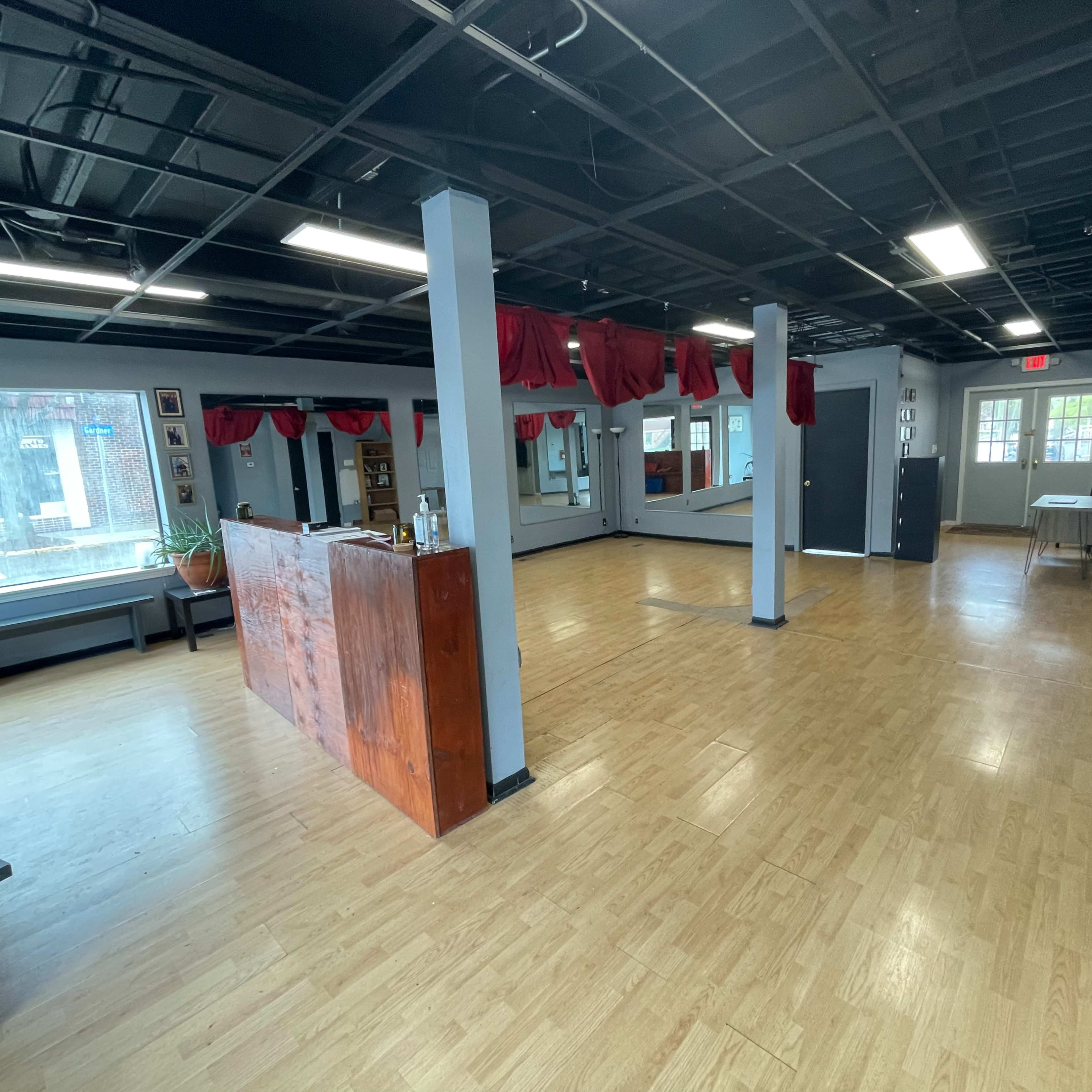 An empty dance studio with wooden flooring, large mirrors, and red drapes hanging from the ceiling.