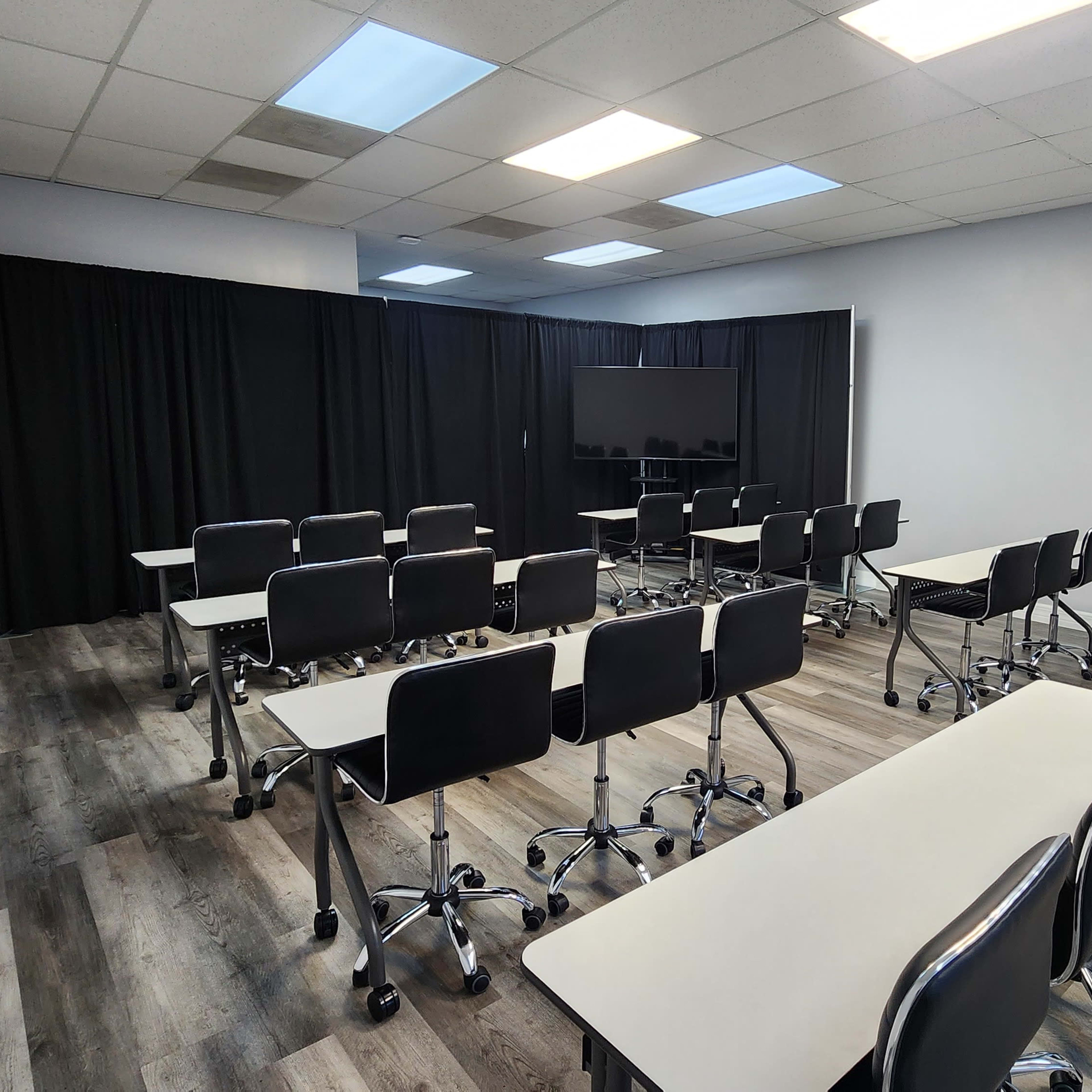 A classroom with rows of desks and chairs arranged facing a large screen, separated by black curtains at the back.