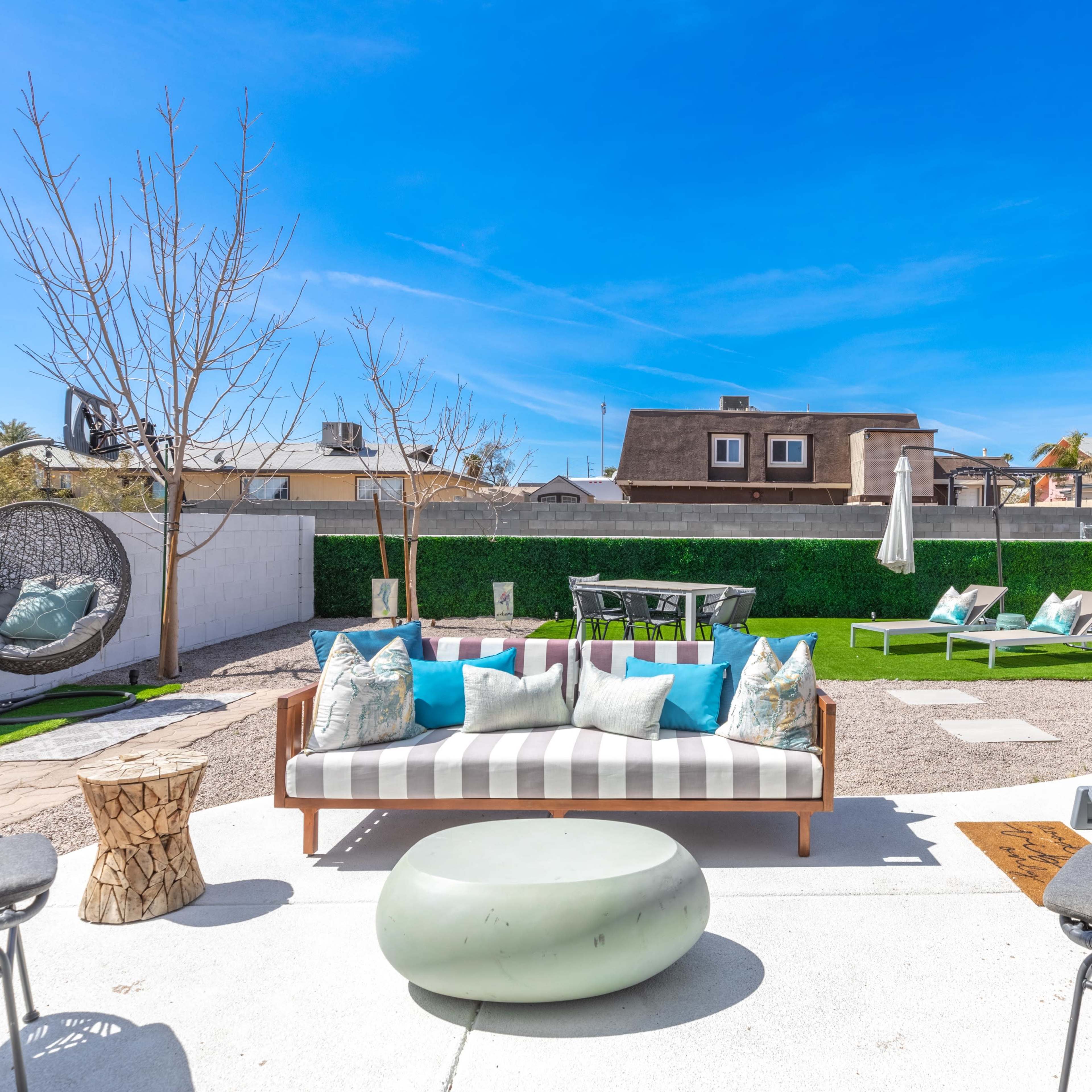 An outdoor patio area with modern seating, a fire pit, and green landscaping.