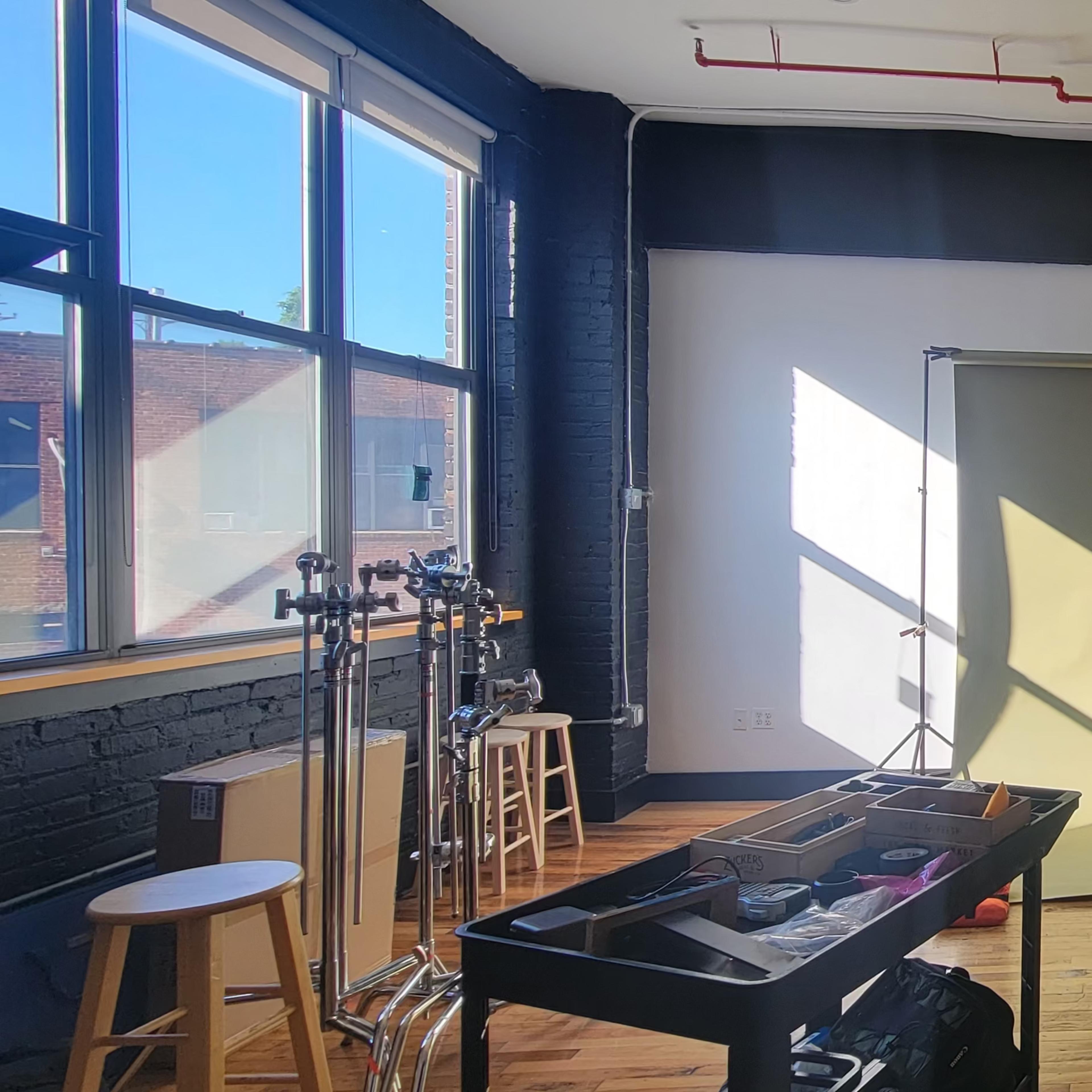 A photo studio with a green backdrop, studio equipment, and a green couch, illuminated by sunlight through large windows.