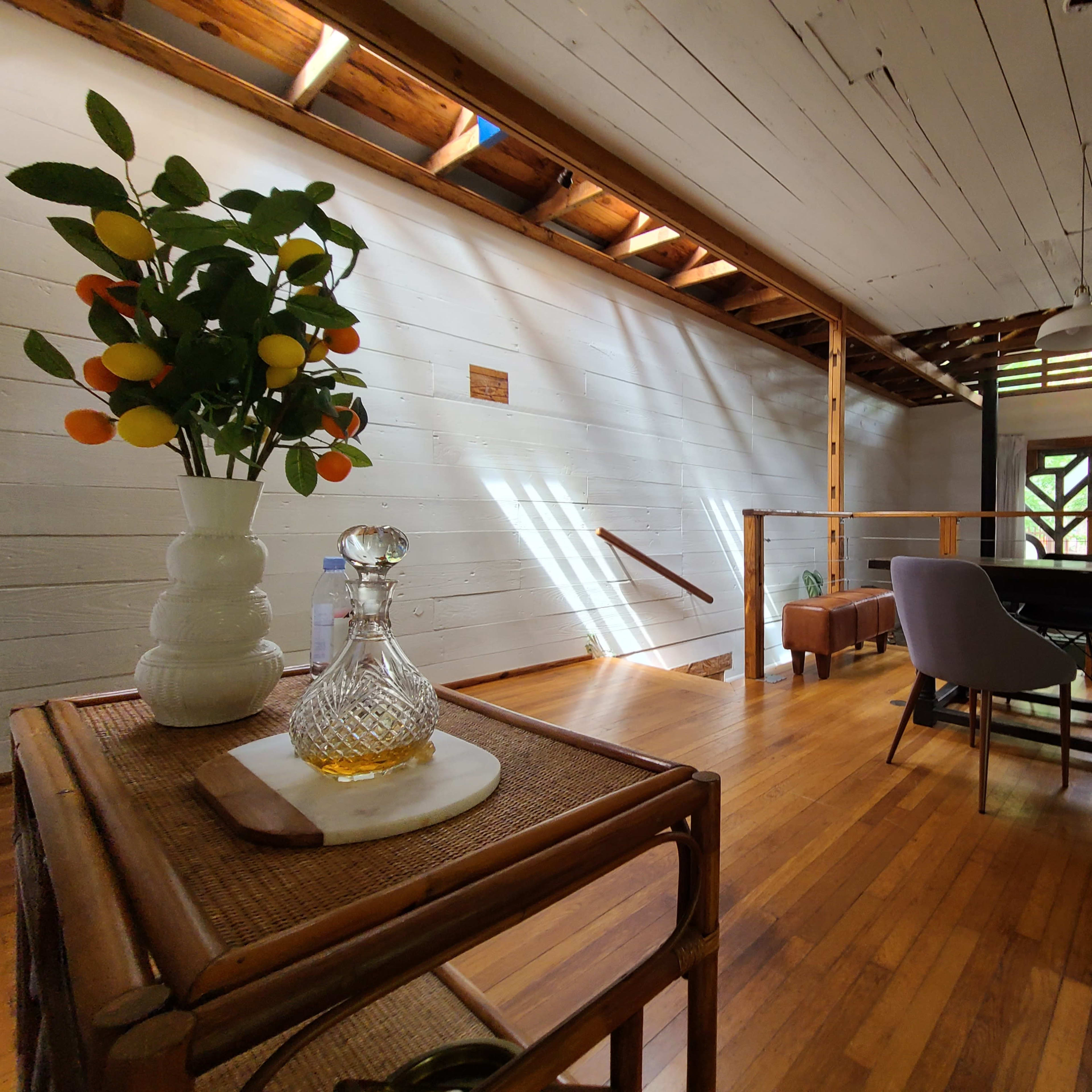 A modern interior space with wooden floors, a dining table, a staircase, and a decorative vase with fruit on a side table.