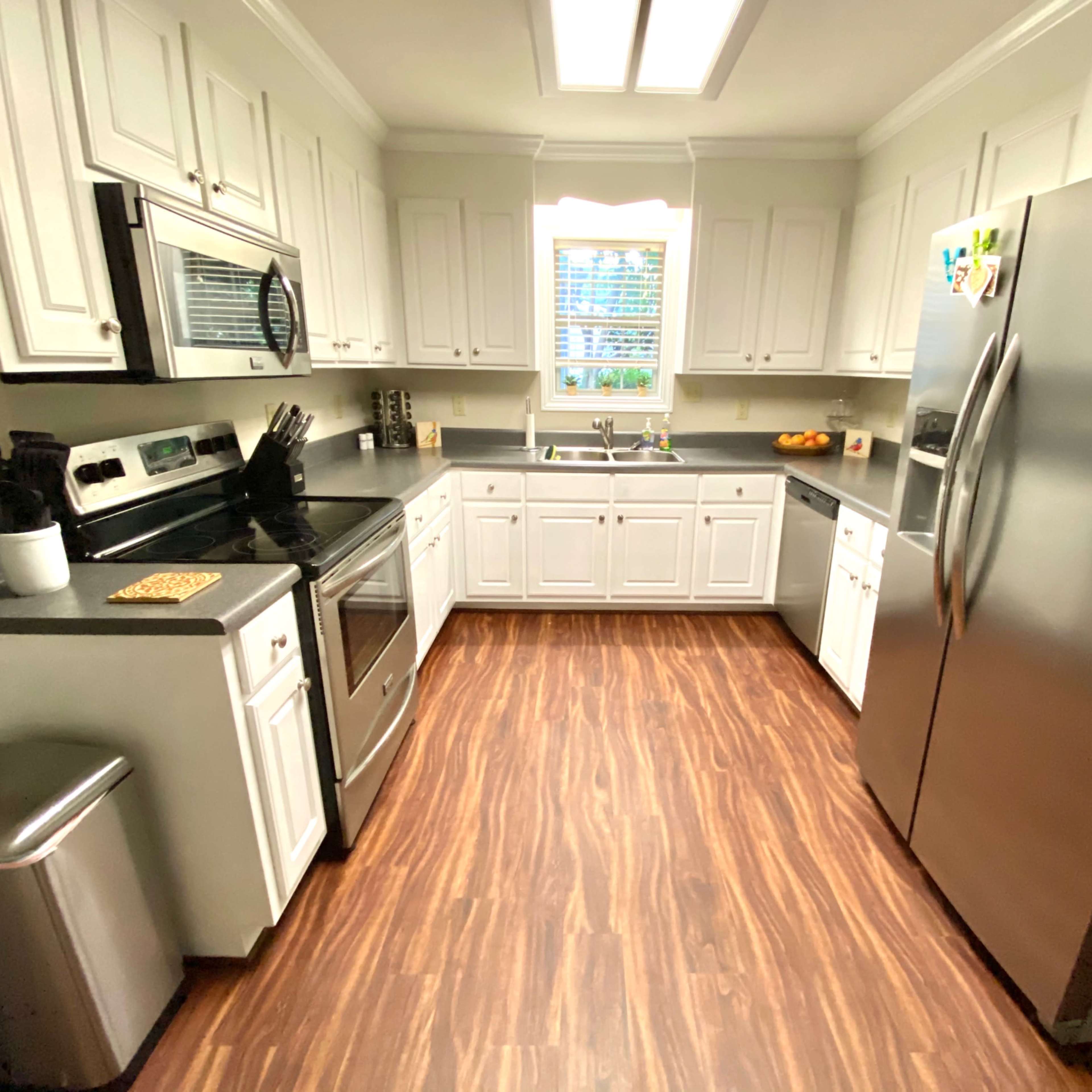 A modern kitchen with white cabinets, stainless steel appliances, and a wooden floor.