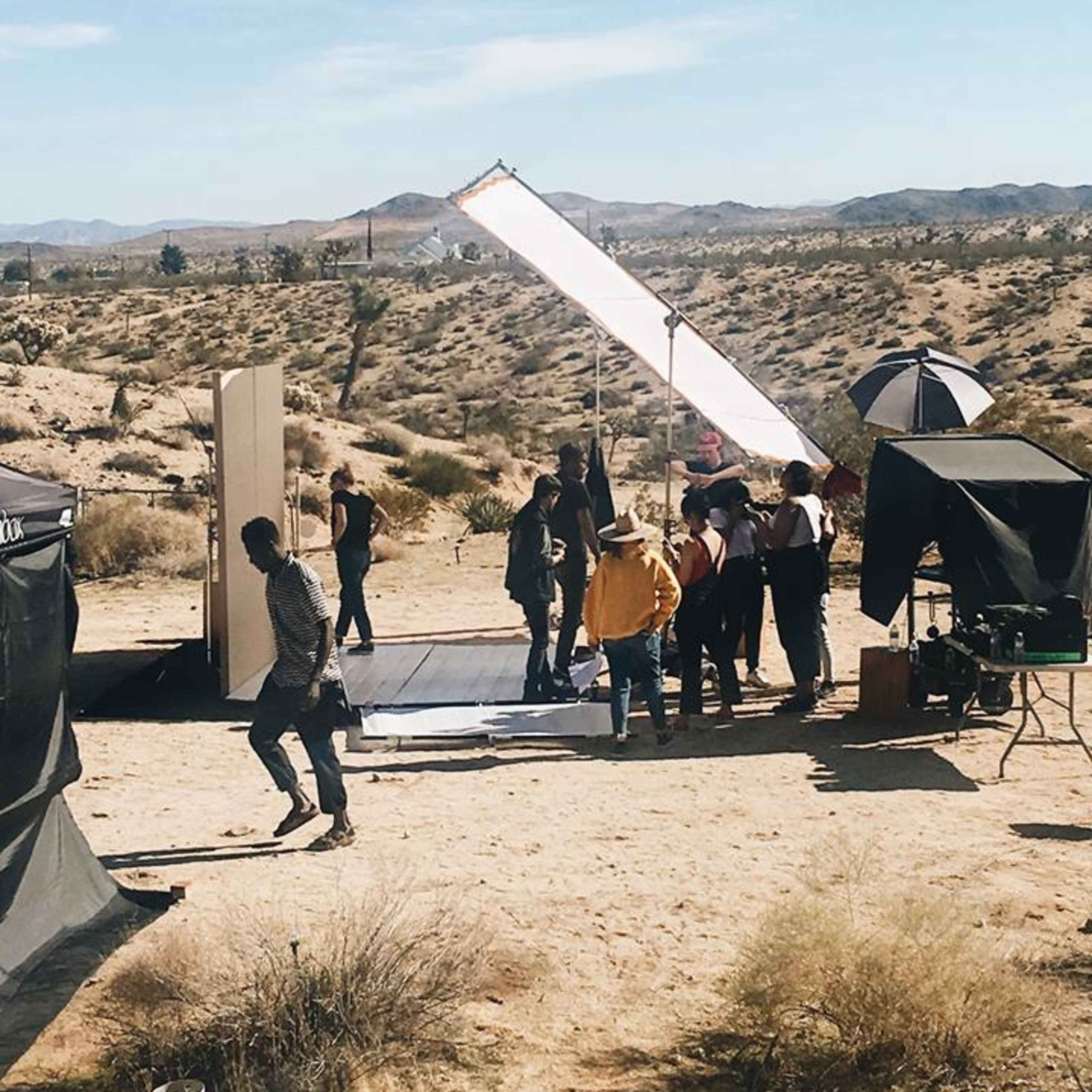 A group of people is setting up a photoshoot in a desert landscape with mountains in the background.
