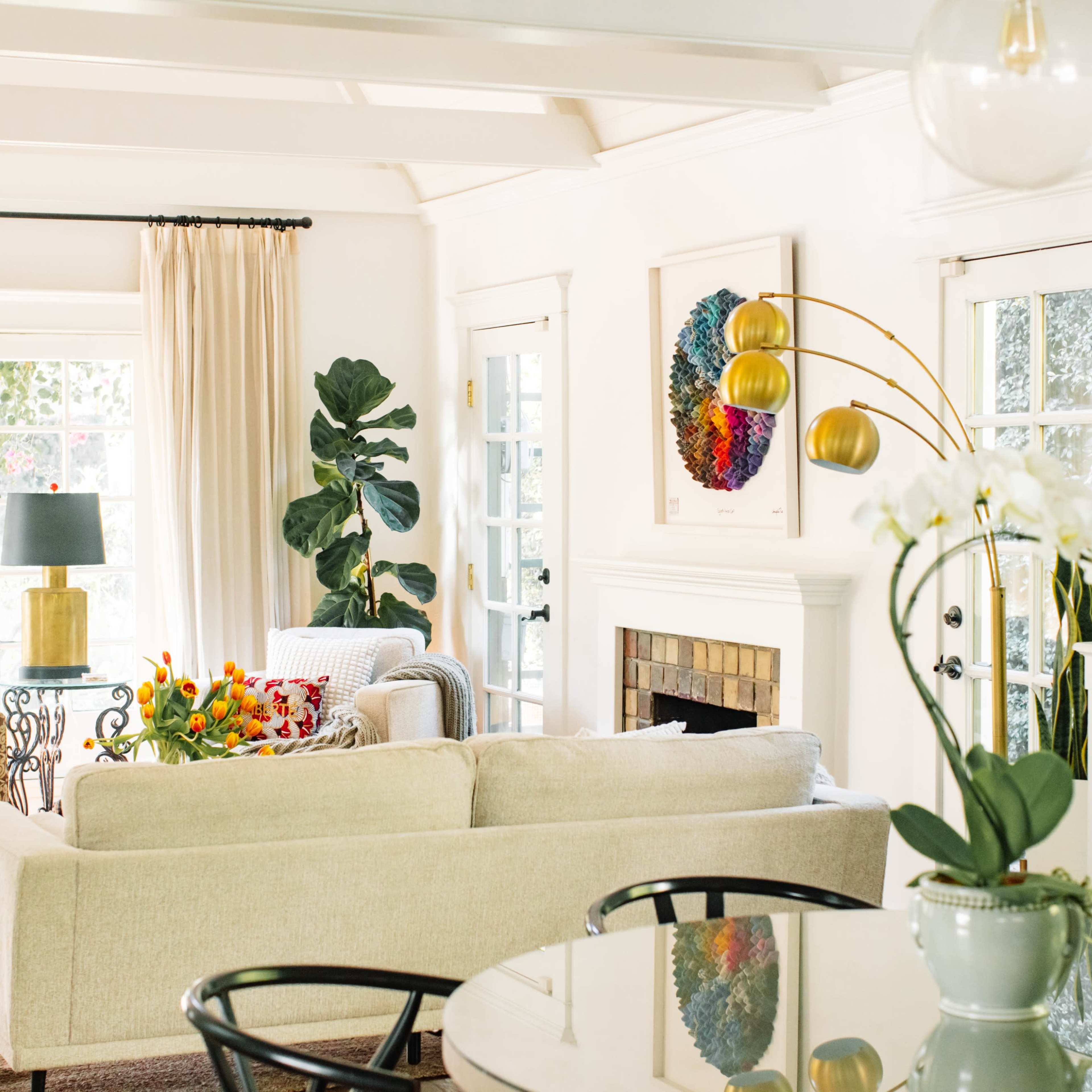 A bright living room with a beige sofa, a coffee table, indoor plants, and large windows letting in natural light.