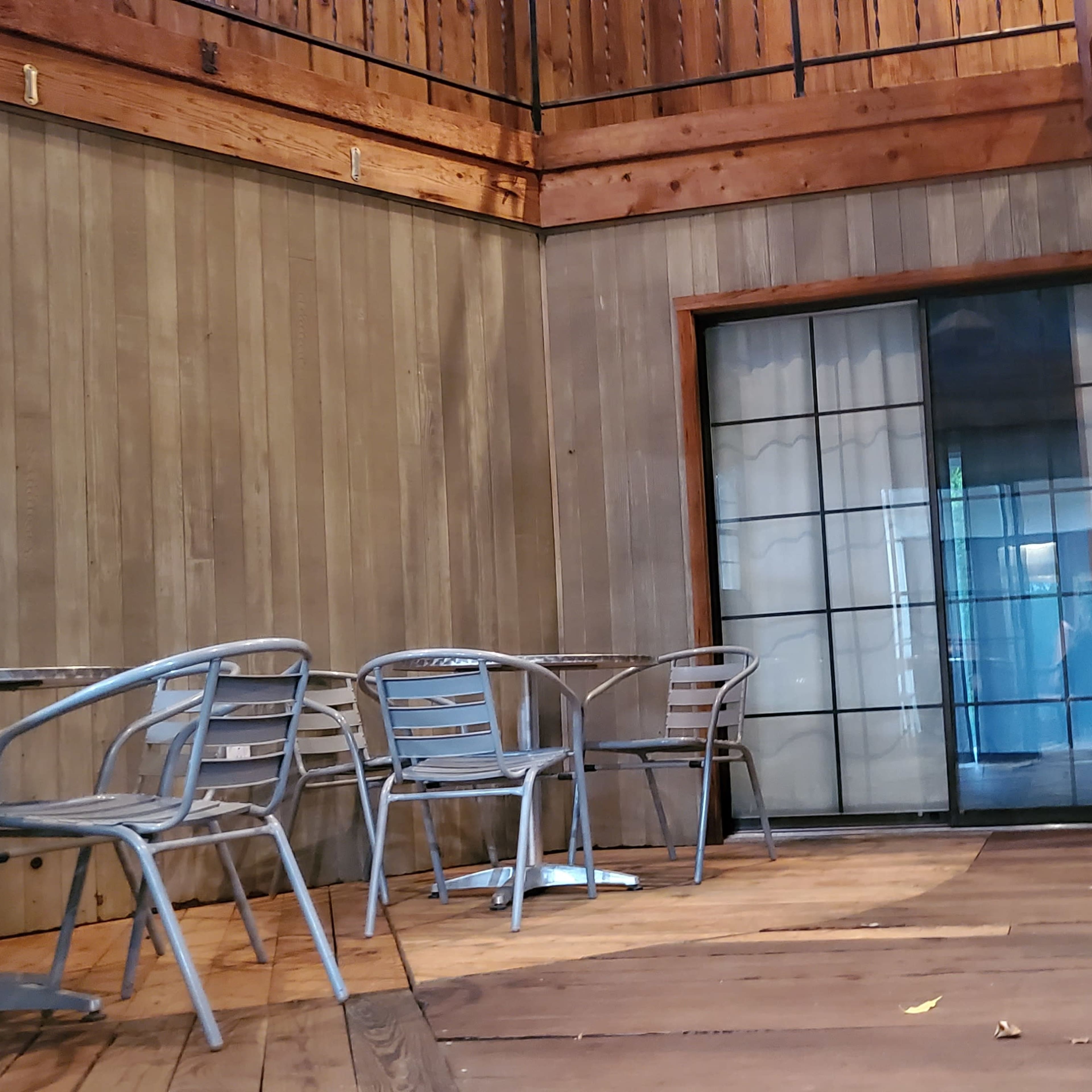 A wooden deck area with several metal chairs and tables arranged near a glass door.
