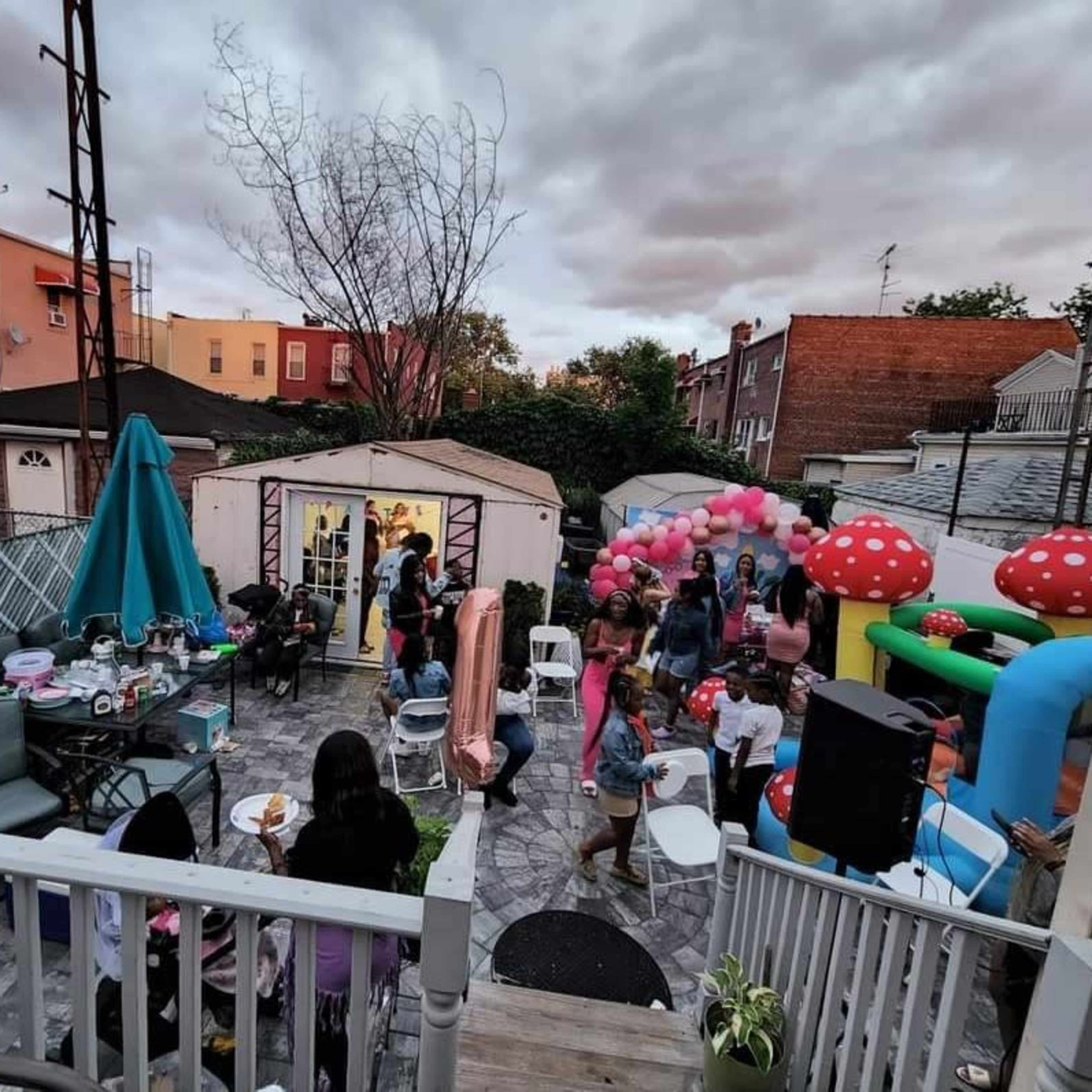 A backyard party is taking place, featuring colorful decorations, various seating arrangements, and several guests enjoying the festivities.
