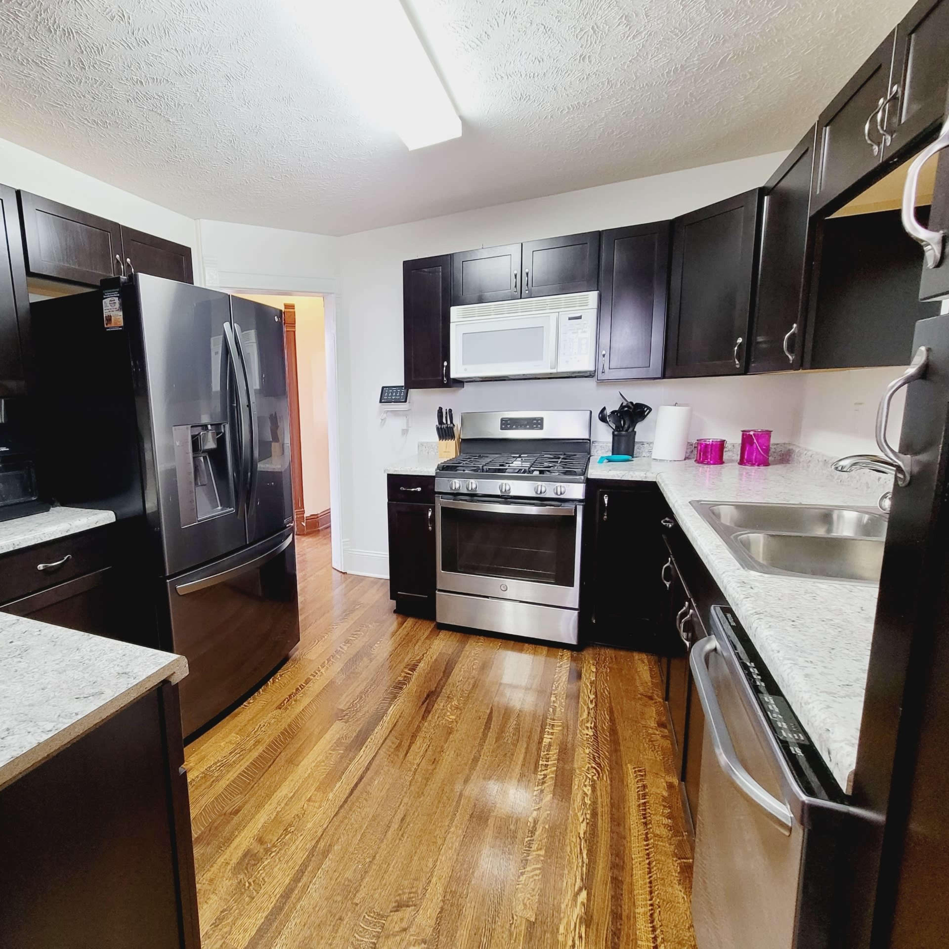 A modern kitchen features dark cabinetry, stainless steel appliances, and granite countertops with hardwood flooring.